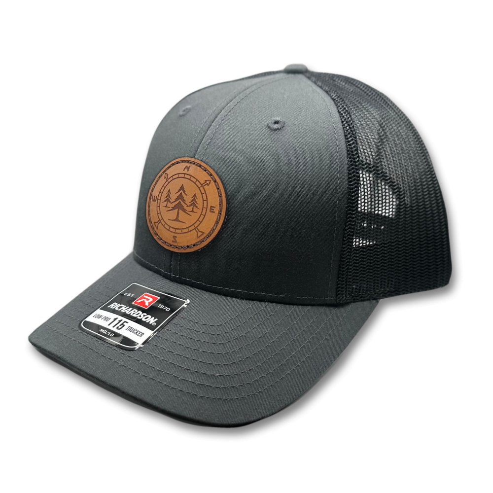 Side view of the Lost Pine Hat in Charcoal/Black, featuring the structured low-profile design, breathable mesh back, and classic pre-curved visor. The hat’s leather patch with a compass and pine trees design is hand-stitched for added durability and style.