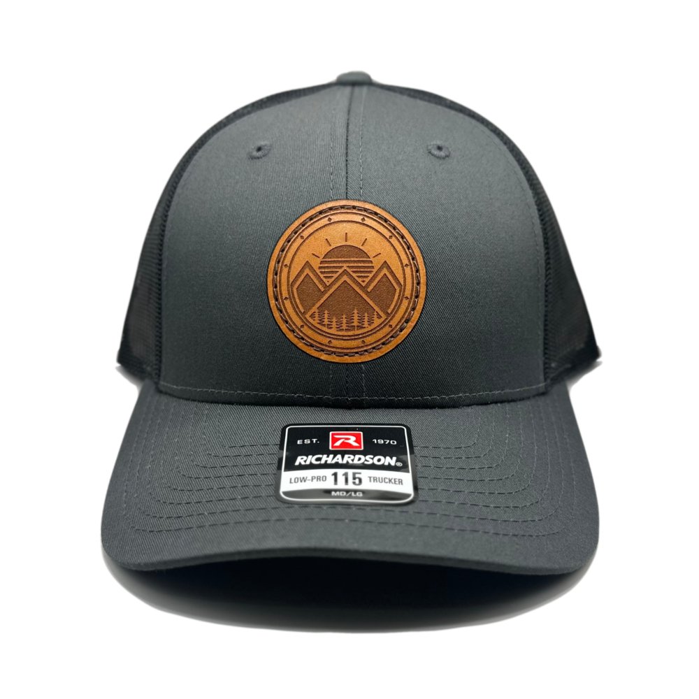 Front view of the Modern Mountains Leather Patch Hat in Charcoal/Black by Outer Wings, featuring a genuine leather patch with a laser-engraved modern mountains and sunset design. The Richardson 115 Low Profile Hat combines a structured six-panel build with a breathable mesh back and adjustable SnapBack closure.