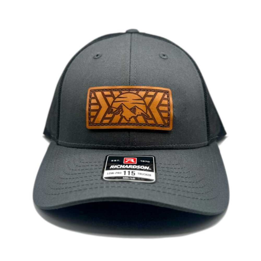 Front view of the Mosaic Mountain Leather Patch Hat by Outer Wings in charcoal/black, crafted on a low profile Richardson 115 hat. This custom leather patch hat features a square leather patch with a laser-engraved mountain and sunset design, making it an excellent outdoors hat with a comfortable fit and adjustable SnapBack closure.