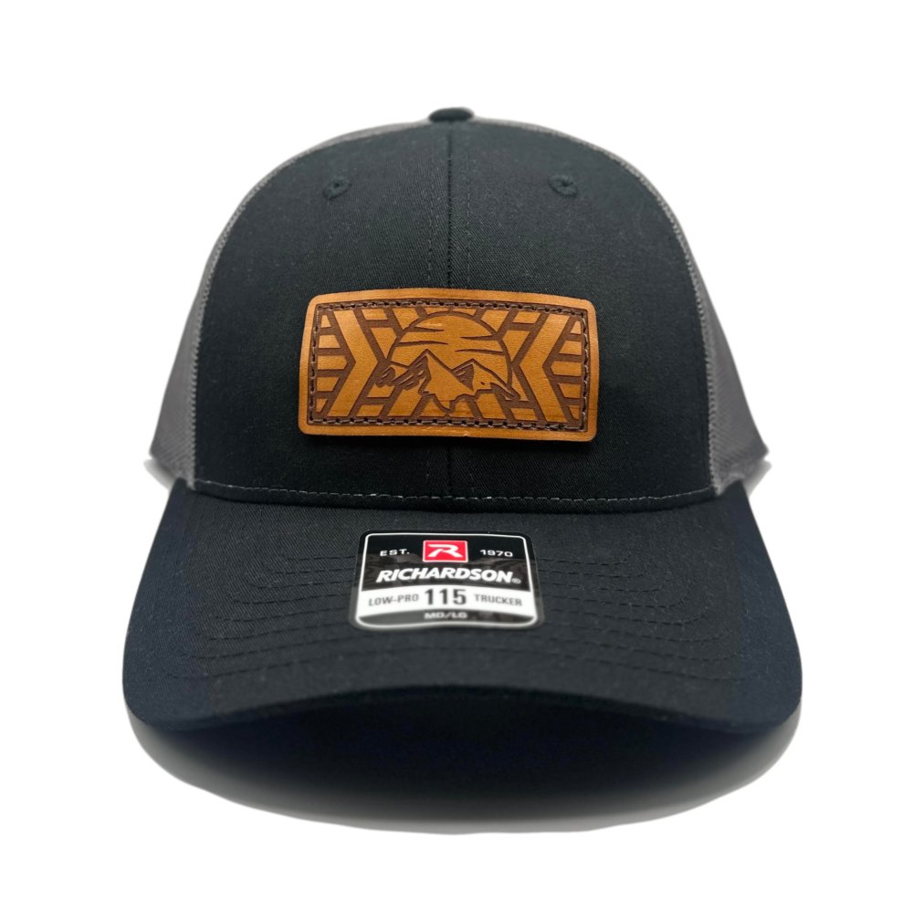 Front view of the Mosaic Mountain Leather Patch Hat by Outer Wings in black/charcoal, on a low profile Richardson 115 hat. This custom leather patch hat features a square leather patch with an engraved mountain and sunset design, combining rugged style with the perfect fit for an outdoors hat. The adjustable SnapBack closure ensures comfort for all head sizes.