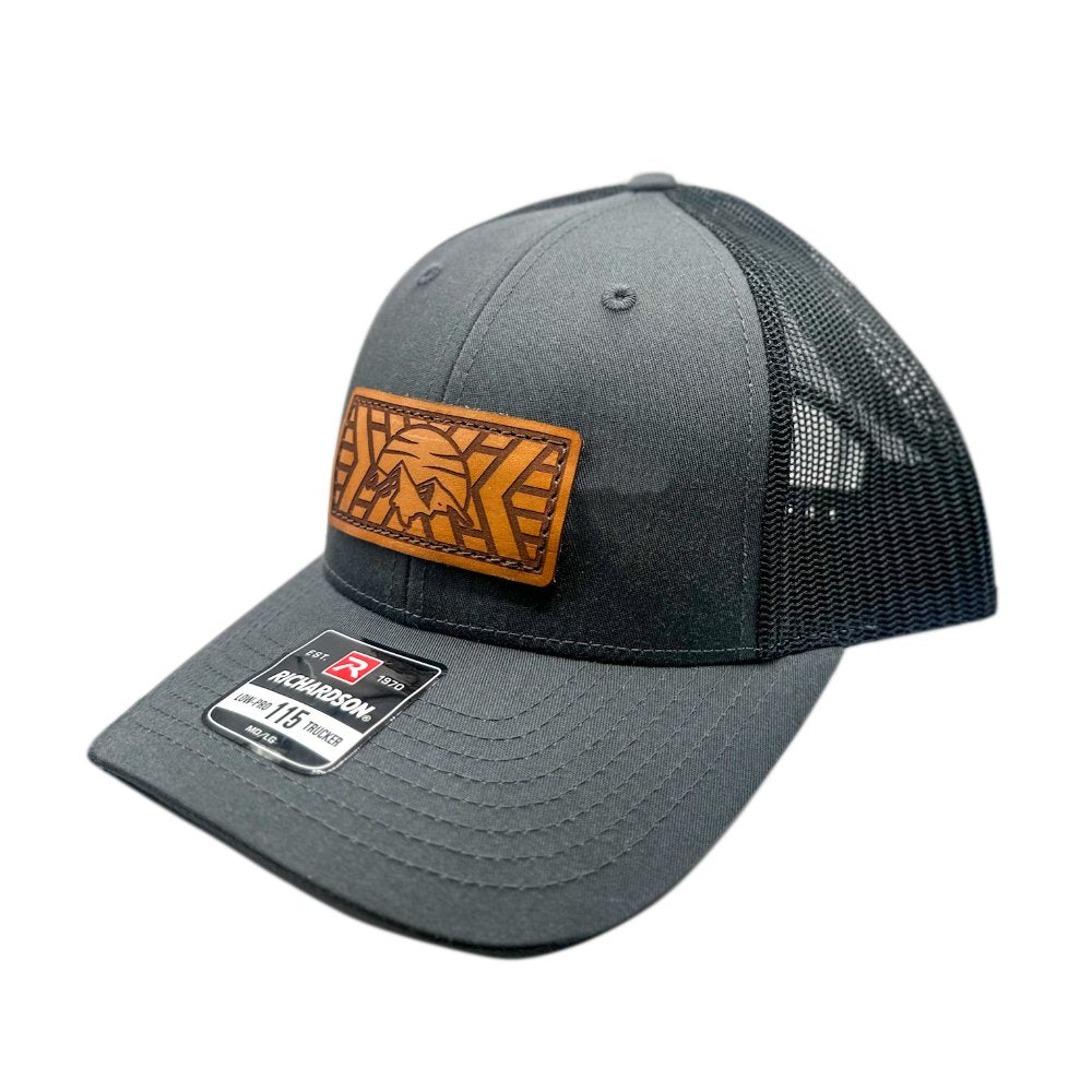 Side view of the Mosaic Mountain Leather Patch Hat by Outer Wings in charcoal/black, showcasing the structured low profile of the Richardson 115 hat. The detailed leather patch with a mountain and sunset engraving adds a rugged touch, perfect for those seeking a high-quality custom leather patch hat for outdoor adventures.