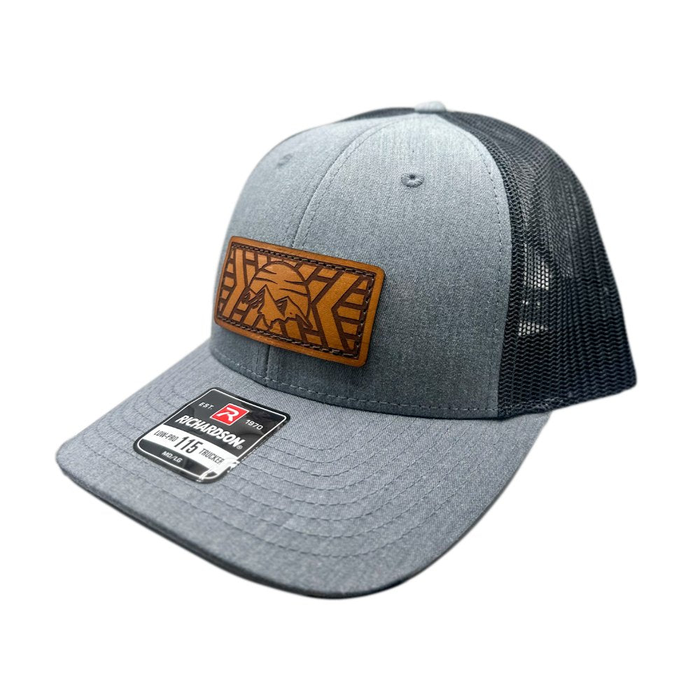 Side view of the Mosaic Mountain Leather Patch Hat by Outer Wings in heather grey/black, highlighting the low profile design of the Richardson 115. The side showcases the laser-engraved leather patch with a mountain and sunset design, making this hat an ideal choice for those looking for a stylish and durable outdoors hat.