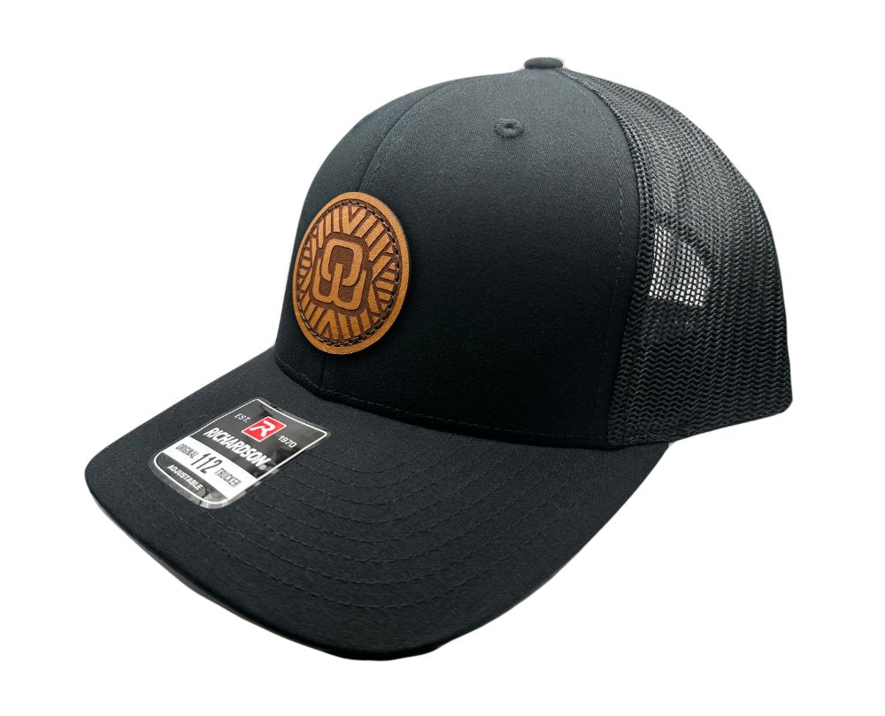 Side view of the Mosaic Wings Leather Patch Hat by Outer Wings in black/black, highlighting the structured mid-profile design of the Richardson 112. The unique leather patch with the Mosaic Wings design adds a rugged and stylish touch to this custom leather patch hat, ideal for everyday wear and outdoor adventures. The mesh back and adjustable SnapBack ensure breathability and a secure fit