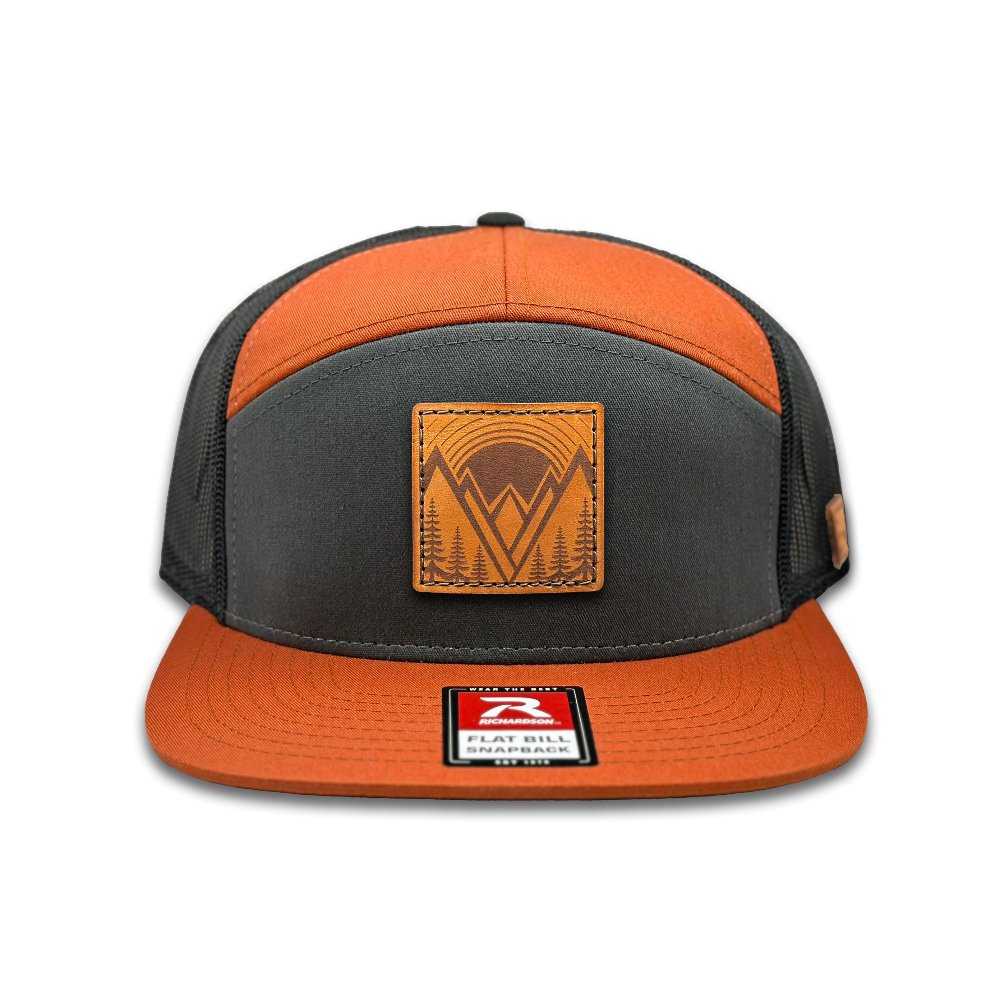 Front view of the Richardson 168 Flat-Bill Trucker Hat in charcoal/burnt orange/black, highlighting its seven-panel, high-profile design. This hat features a flat bill, a cotton/nylon/polyester blend front, and a polyester mesh back, offering a bold look and adjustable SnapBack fit for any adventure.