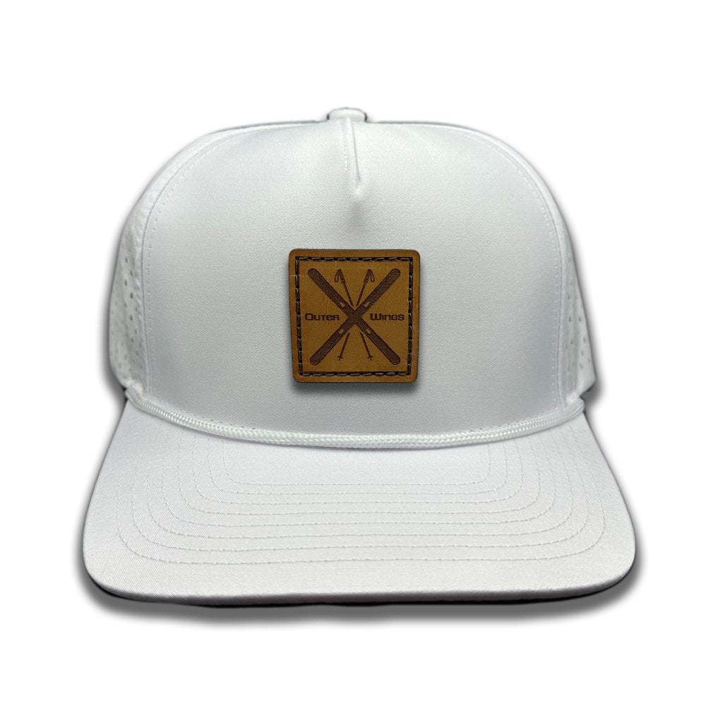 Front view of the Alpine Wings Hat by Outer Wings in white, featuring a high-profile Outer Wings 970 hat with a square leather patch of crossed skis and the words 'Outer Wings.' The hat showcases a water-resistant fabric, structured build, and classic rope detail, perfect for mountain adventures.