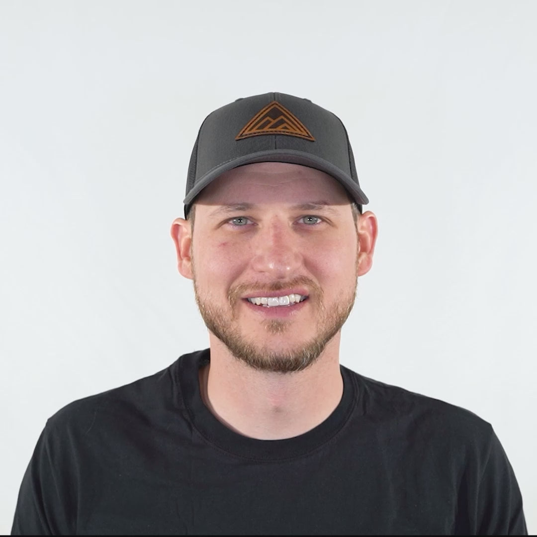 Video of model wearing Dark Mountain leather patch hat on charcoal and black Richardson 115 low profile trucker, turning head left and right to show the mountain patch, curved bill, mesh back, and snapback fit.

Color: Charcoal/Black
