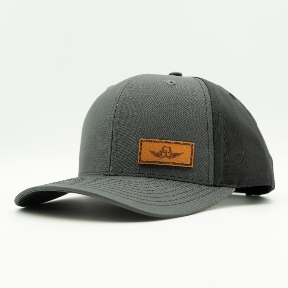 Side view of charcoal/black Richardson 312 hat with Spread Your Wings leather patch, curved visor, snapback.