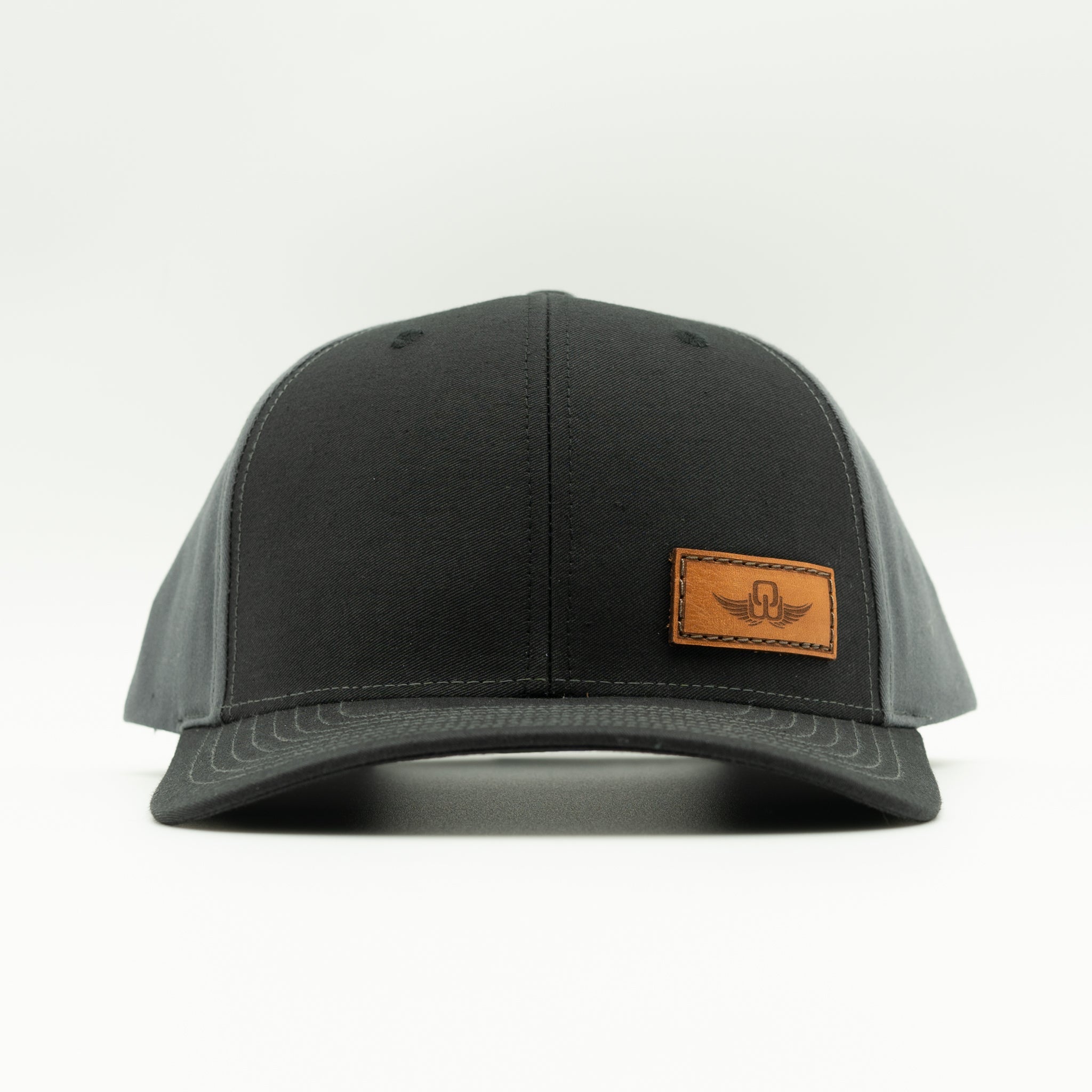Front view of black/charcoal Richardson 312 snapback with sewn Spread Your Wings leather patch and mid profile fit