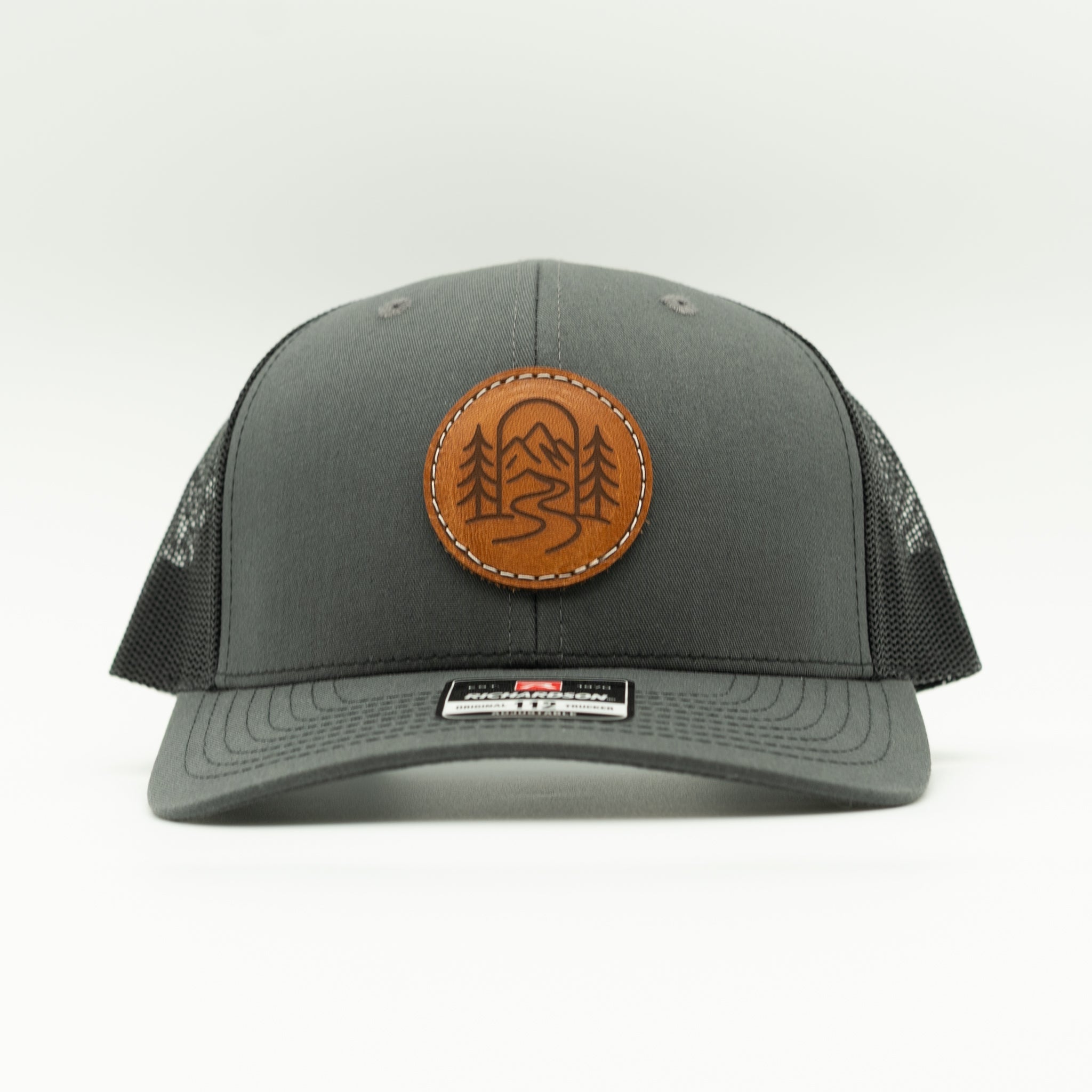Front view of charcoal and black Richardson 112 The Passage hat with round veg tan leather mountain design.