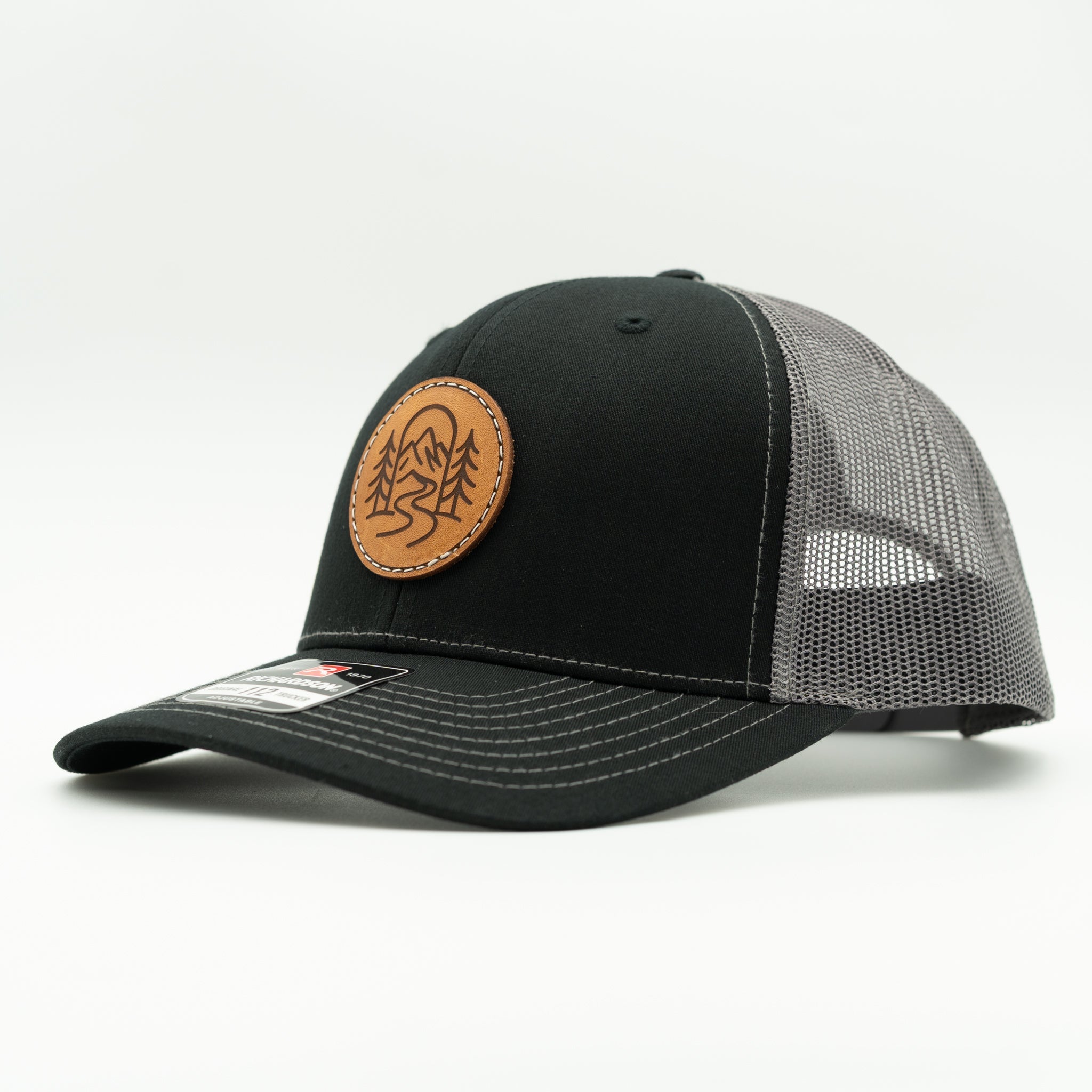 Side view of The Passage black and charcoal Richardson 112 leather patch outdoor trucker hat.