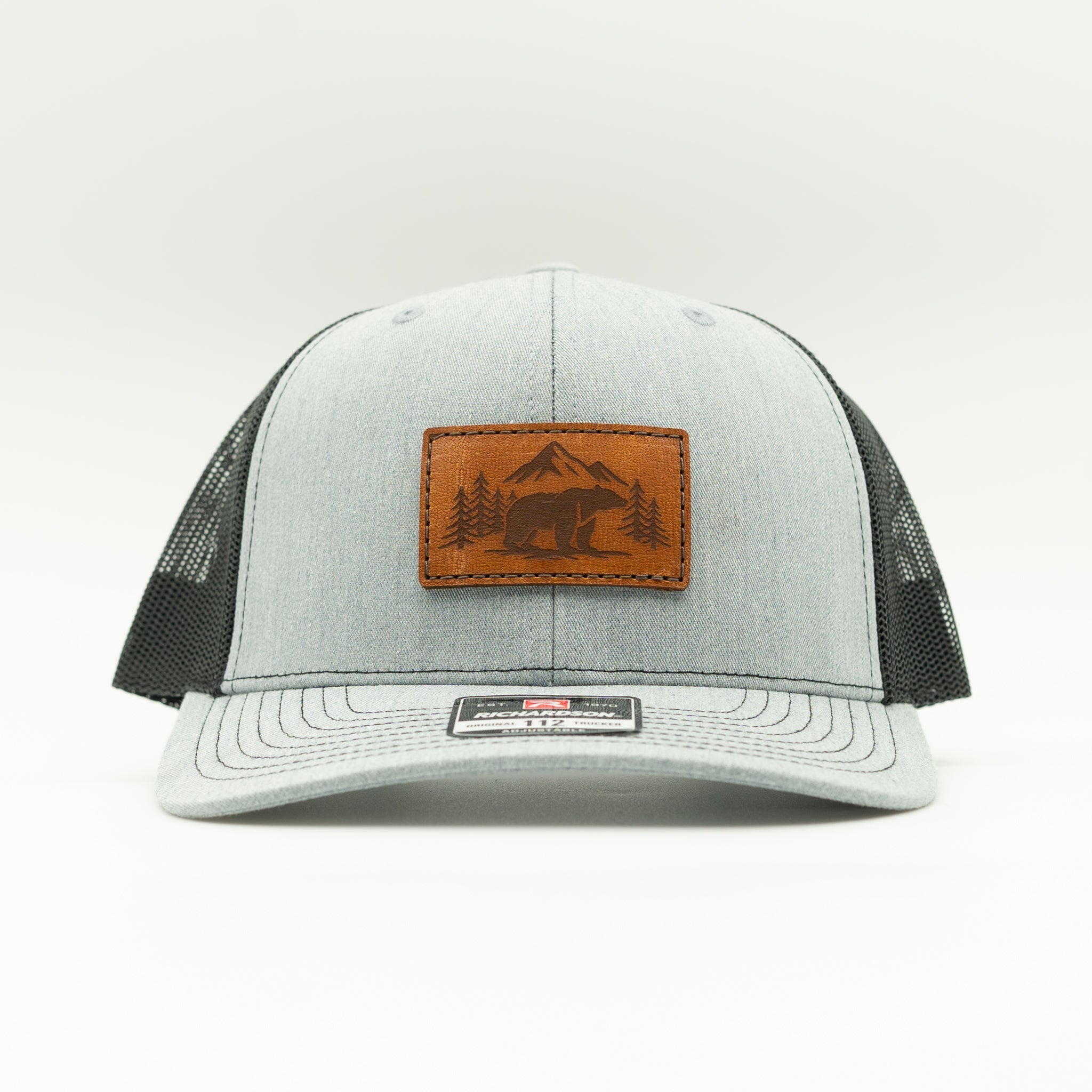 Front view of Bearline Peak leather patch hat on heather grey and black Richardson 112 trucker, showing bear and mountain patch, curved bill, and black mesh back.

Color: Heather Grey/Black