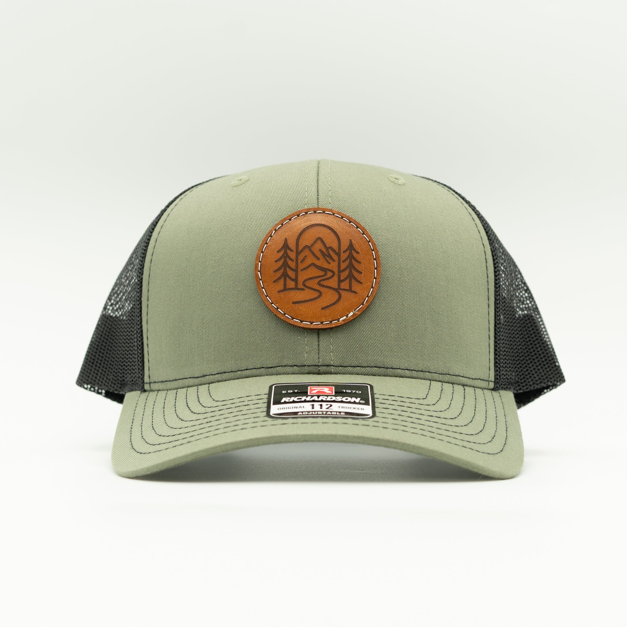 Front view of The Passage loden and black Richardson 112 trucker with round veg tan leather mountain trail patch.