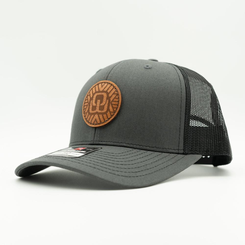 A dark gray trucker cap with a black mesh back and a brown circular leather patch on the front 

Color: Charcoal/Black