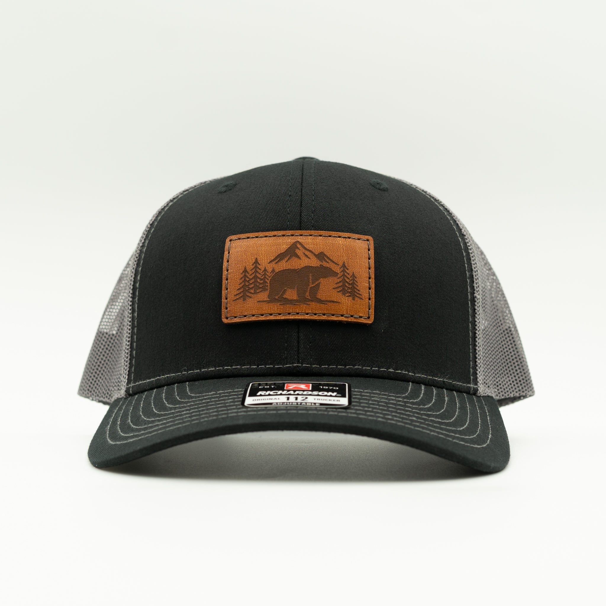 Front view of Bearline Peak leather patch hat on black and charcoal Richardson 112 trucker, showing bear and mountain patch, mid profile crown, curved bill, and mesh back.

Color: Black/Charcoal