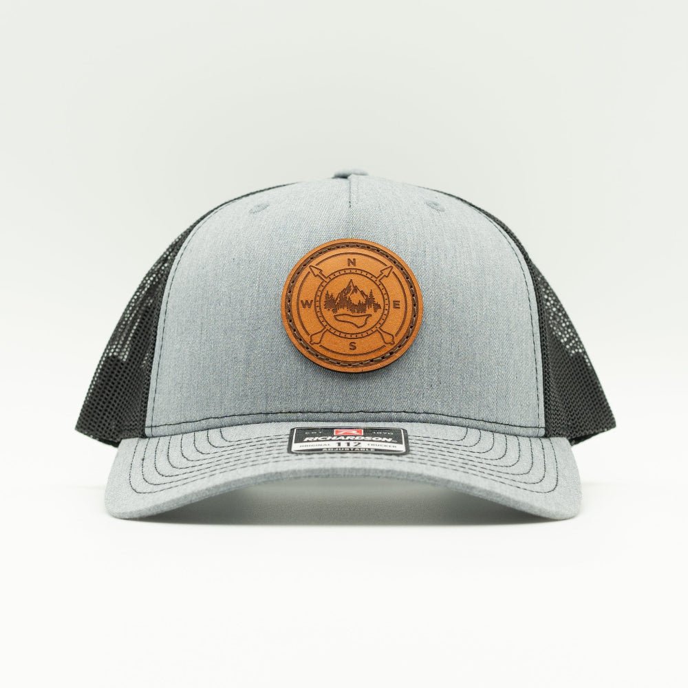 Heather grey and black Richardson 112FP five panel trucker, front view with round compass leather patch stitched on
