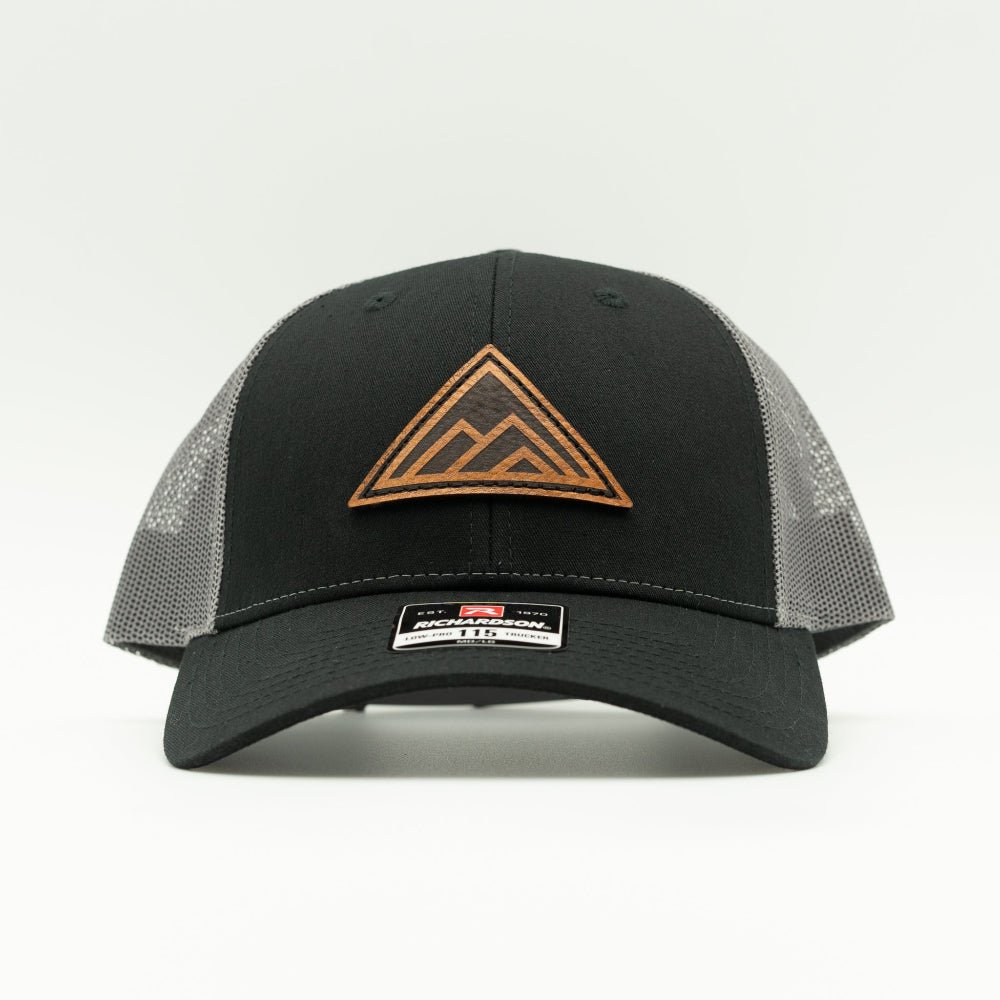 Dark Mountain leather patch hat on a black and charcoal Richardson 115 low profile trucker hat, front view with triangle mountain patch, curved bill, mesh back, and snapback, a low profile mountain hat for everyday wear.

Color: Black/Charcoal