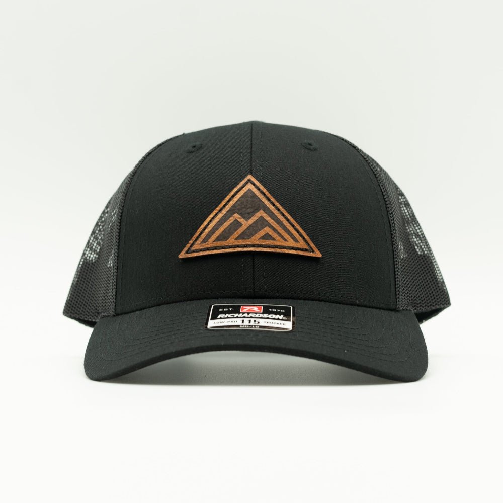 Dark Mountain leather patch hat on a solid black Richardson 115 low profile trucker hat, front view showing triangle mountain patch, curved bill, mesh back, and snapback, a low profile mountain hat for small heads and everyday wear.

Color: Solid Black