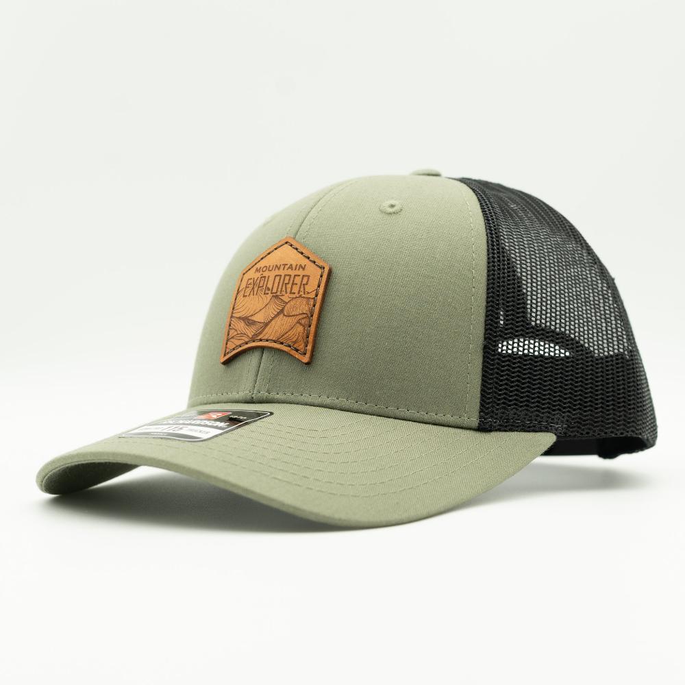 Side profile of Mountain Explorer leather patch hat on loden and black Richardson 115 low profile trucker, showing earthy green front, black mesh, and curved brim.