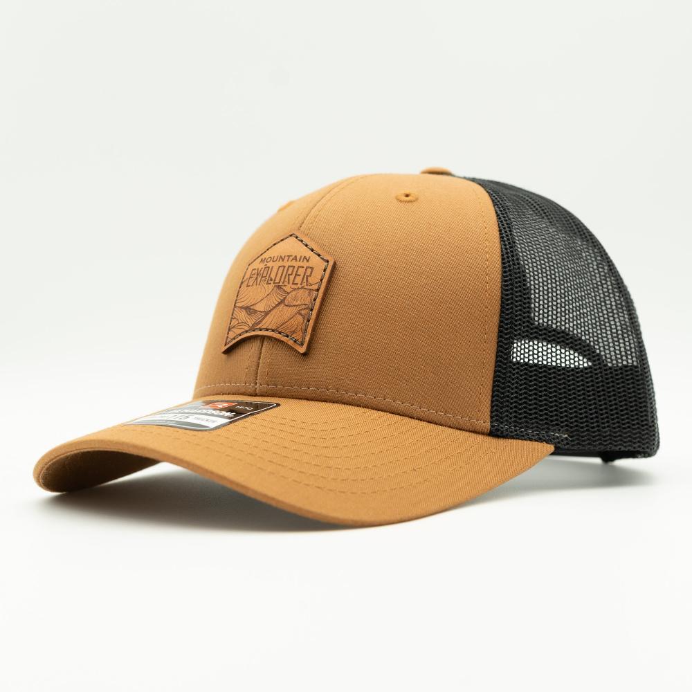 Side view of Mountain Explorer leather patch hat on caramel and black Richardson 115 low profile trucker, warm caramel front panel with black mesh and curved visor.