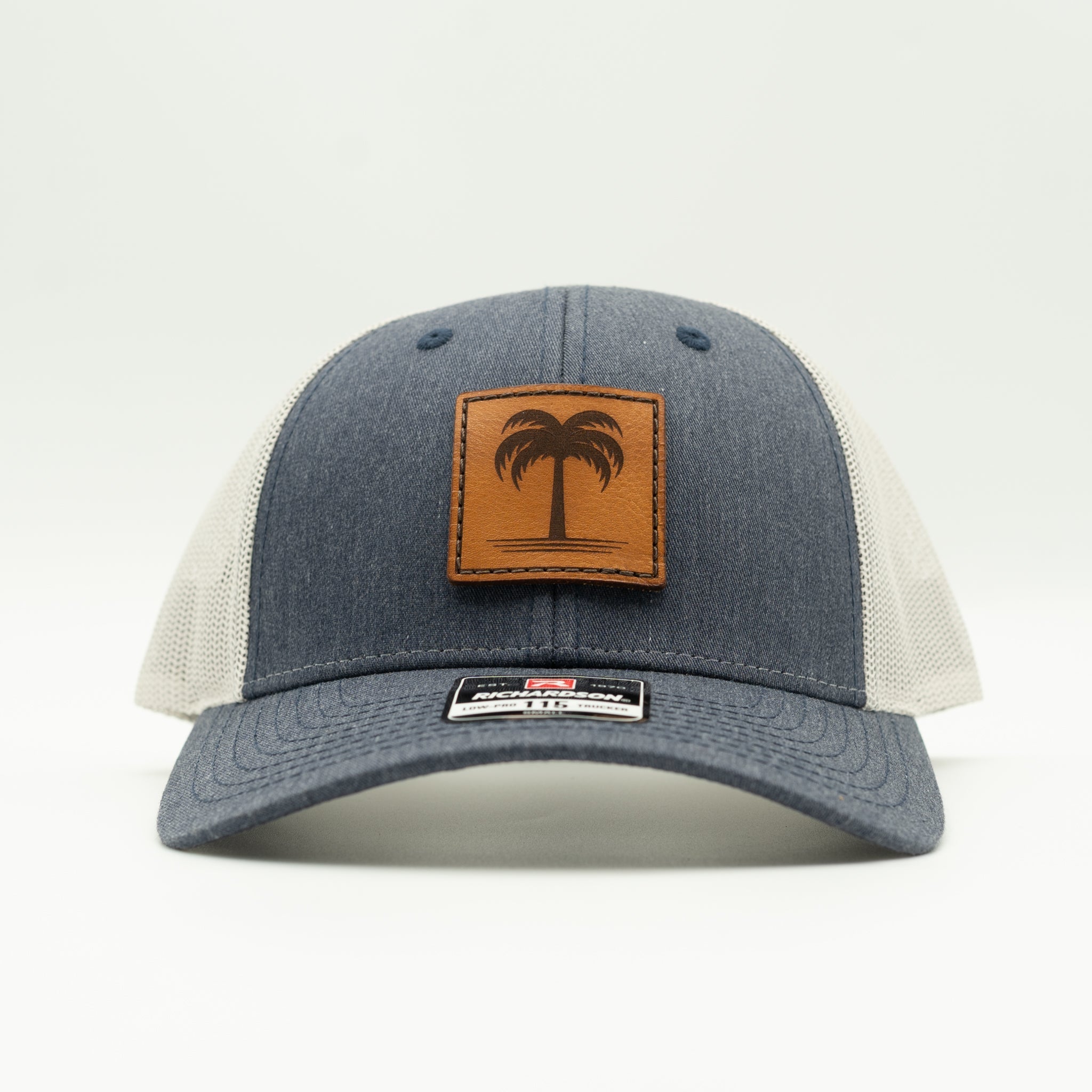 Front view heather navy/grey Solo Palm hat, engraved palm leather patch on a coastal-inspired low profile trucker for beach trips.