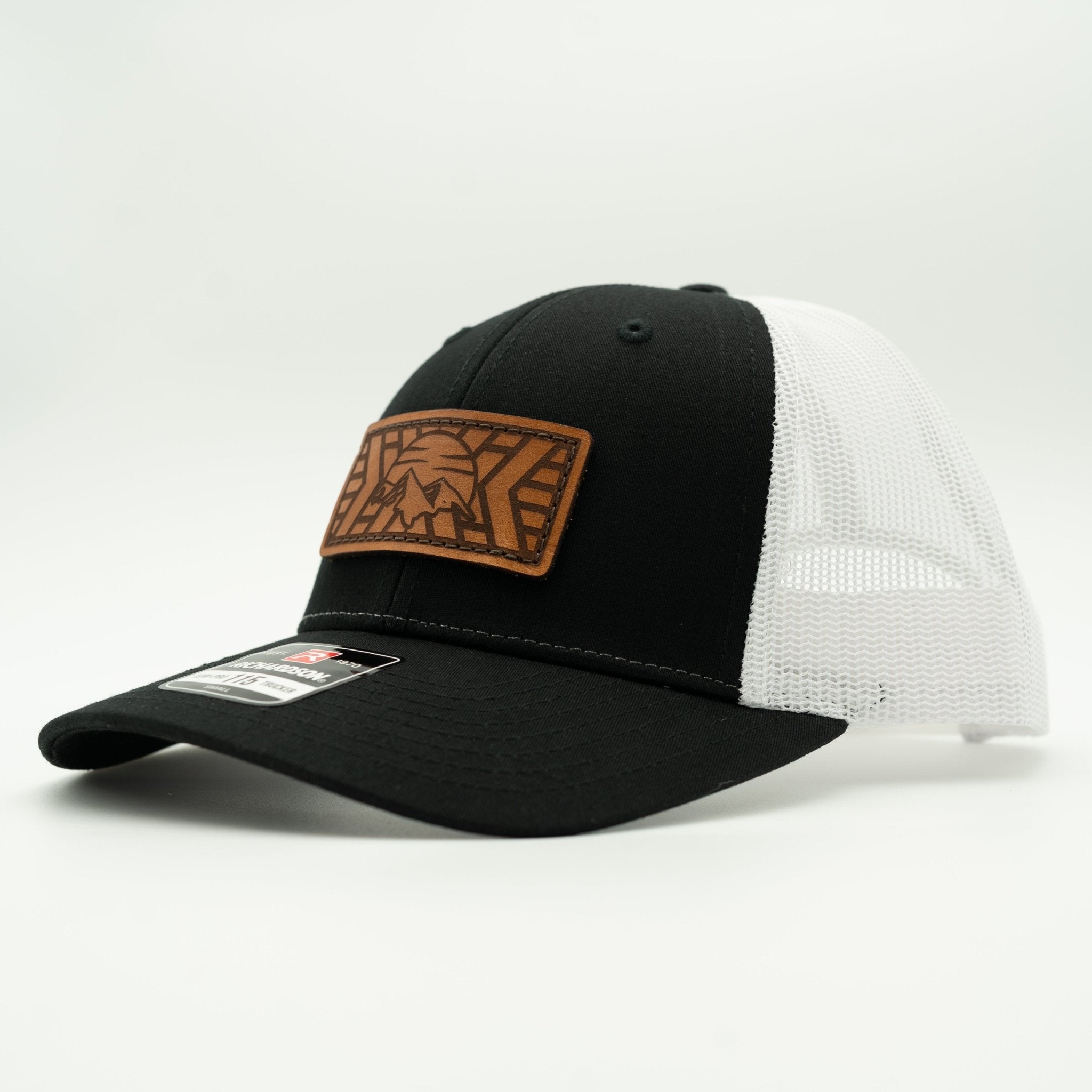 A black and white trucker hat with a brown leather patch on the front, photographed on a clean white background.

Color: Black/White