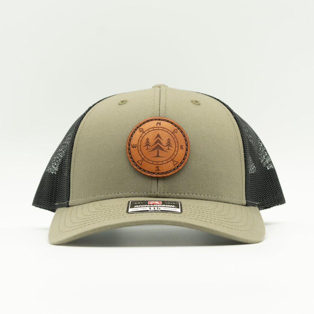 A trucker-style baseball cap in olive green with black mesh back panels and a circular brown leather patch on the front featuring a tree design.

Color: Loden/Black