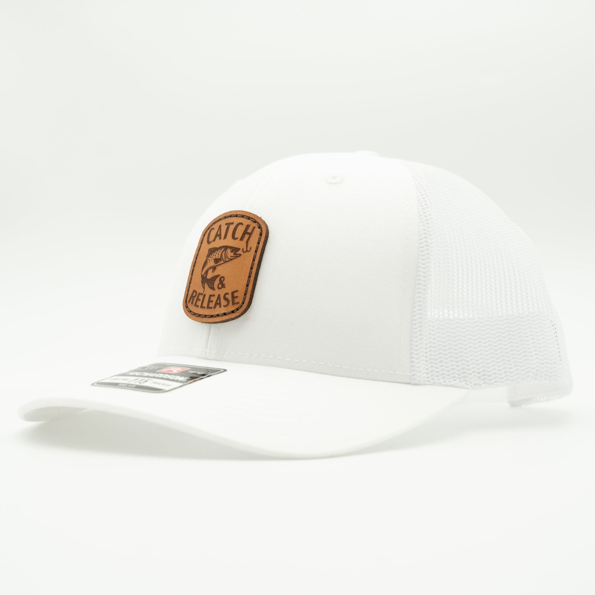 A white trucker-style cap with a brown leather patch on the front that reads 'CATCH RELEASE' with a fish graphic, shown on a clean white background.

Color: Solid White