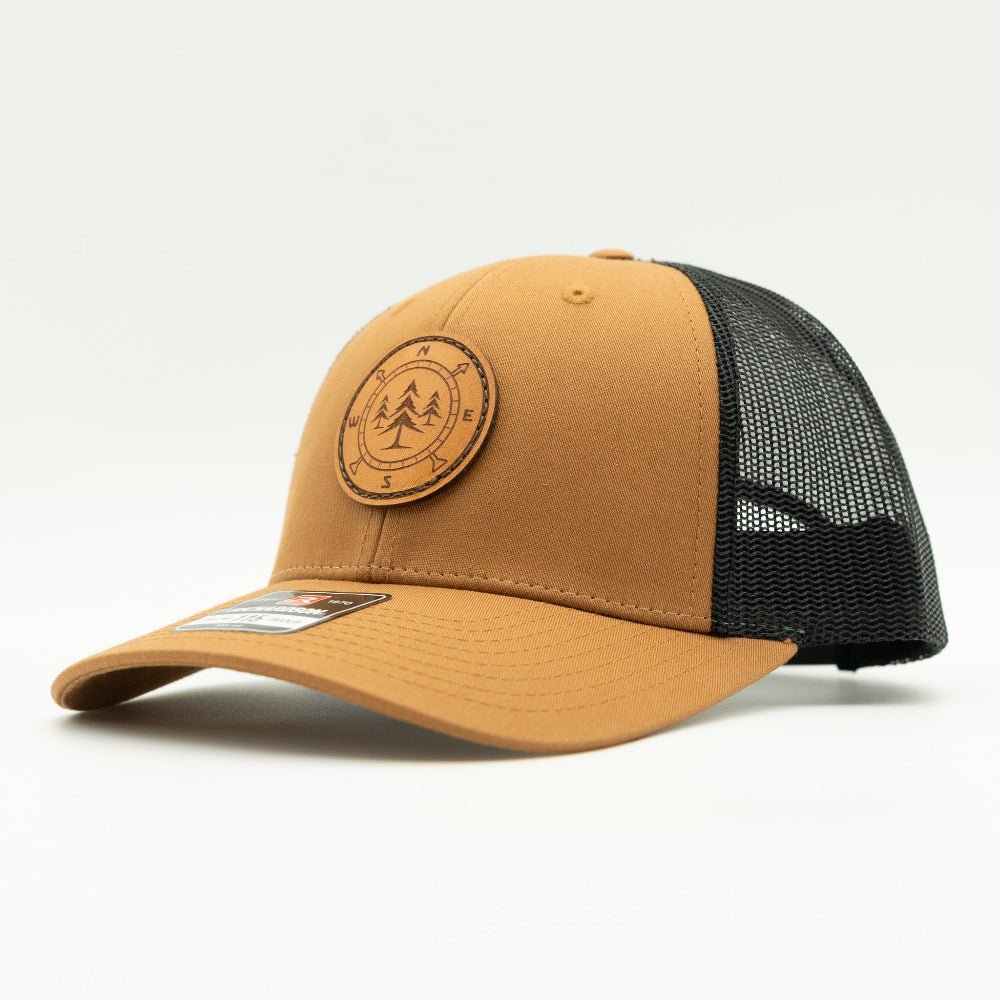 Side view of the Lost Pine Hat in Caramel/Black, showcasing the breathable mesh back, structured profile, and adjustable closure. The hat includes a hand-stitched leather patch with a compass and pine trees design, perfect for those who love the outdoors.

Color: Caramel/Black
