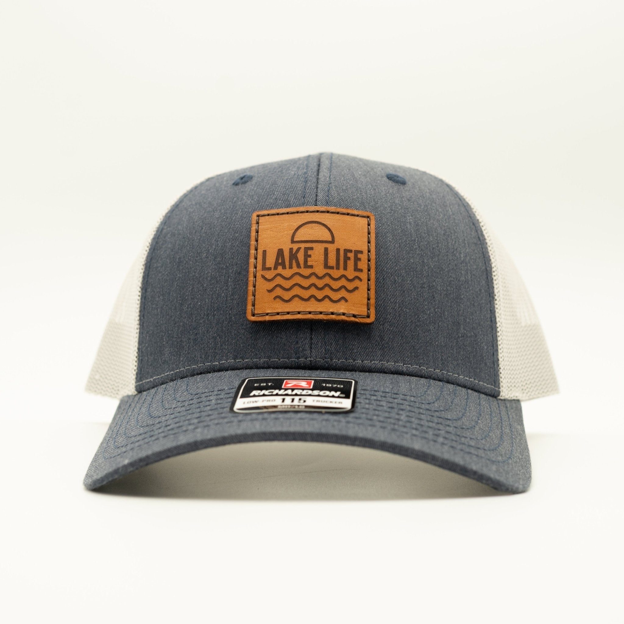 A Heather Navy and greytrucker hat with a brown leather patch on the front that reads 'LAKE LIFE'. The hat is photographed against a clean white background.

Color: Heather Navy/Grey