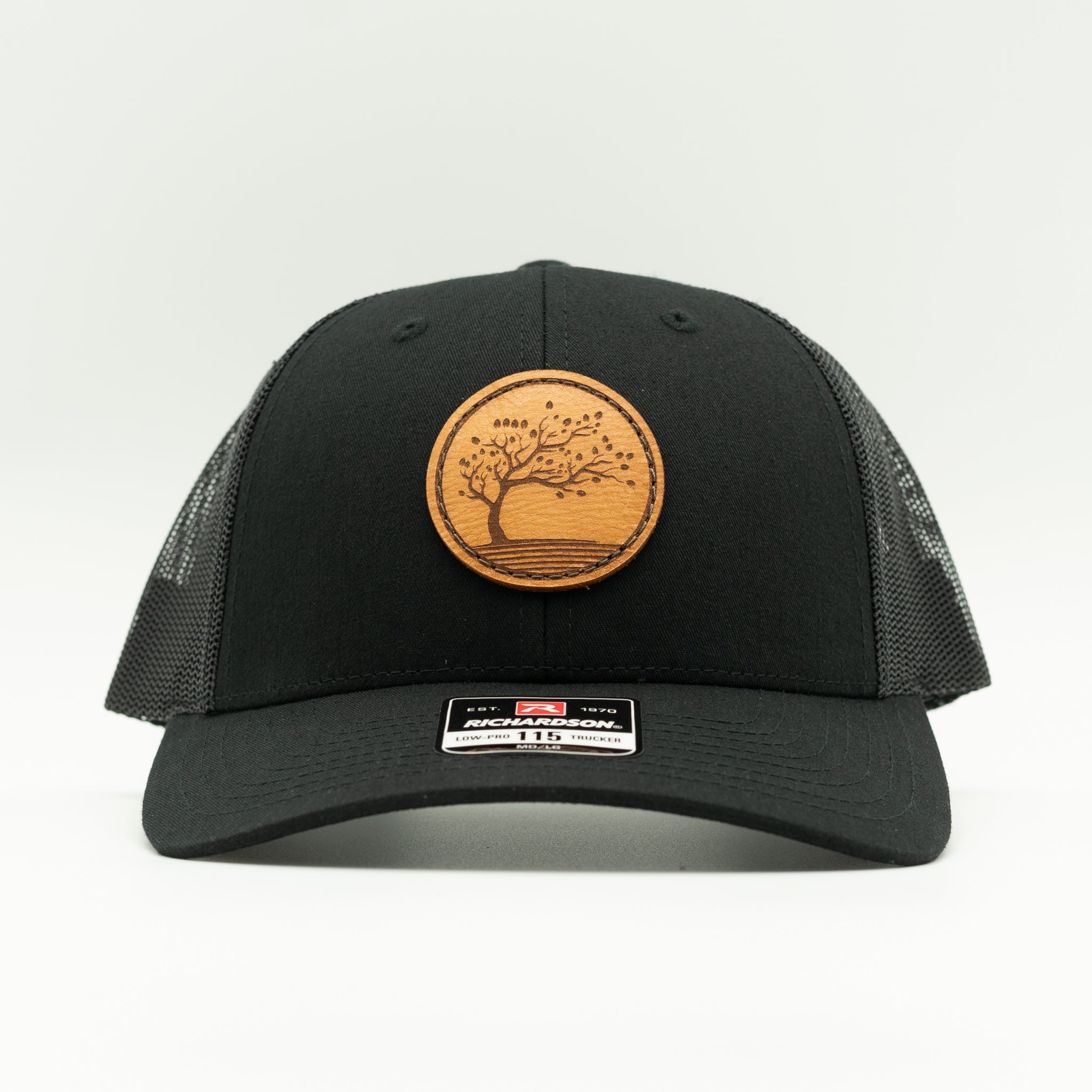 Front view of all black Richardson 115 low profile hat featuring round Blossom engraved leather patch and structured crown.

Color: Solid Black
