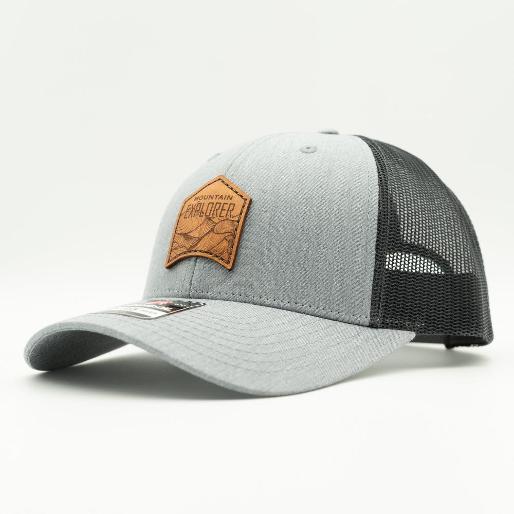 Side profile of Mountain Explorer leather patch hat on heather grey and dark charcoal Richardson 115 low profile trucker, highlighting mesh back and subtle mountain style
