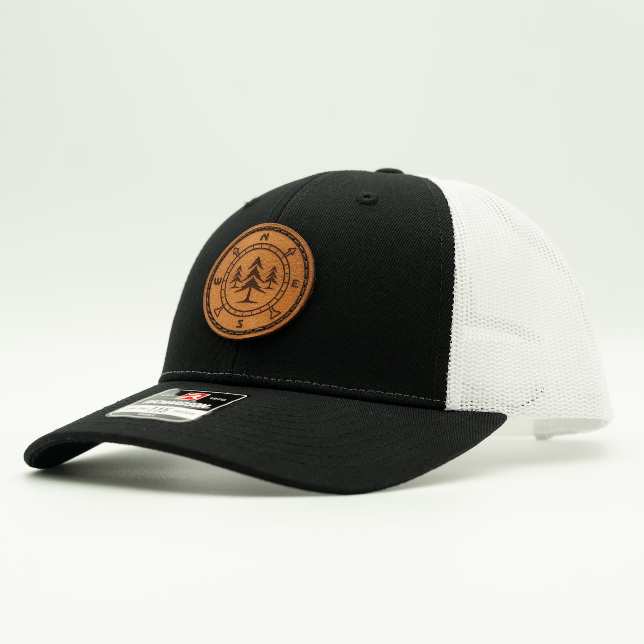 A black and white trucker cap with a brown circular leather patch on the front, photographed on a clean white background.

Color: Black/White