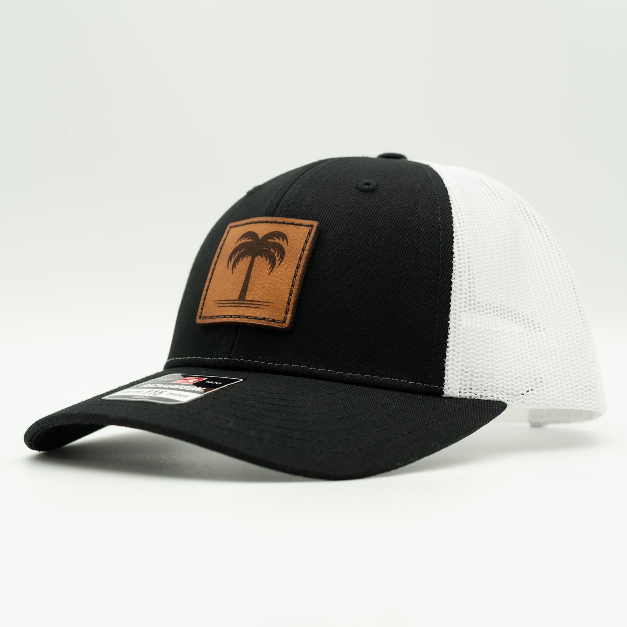 Black and white Solo Palm Richardson 115 low profile trucker hat, side profile with black crown, white mesh, and sewn palm leather patch.