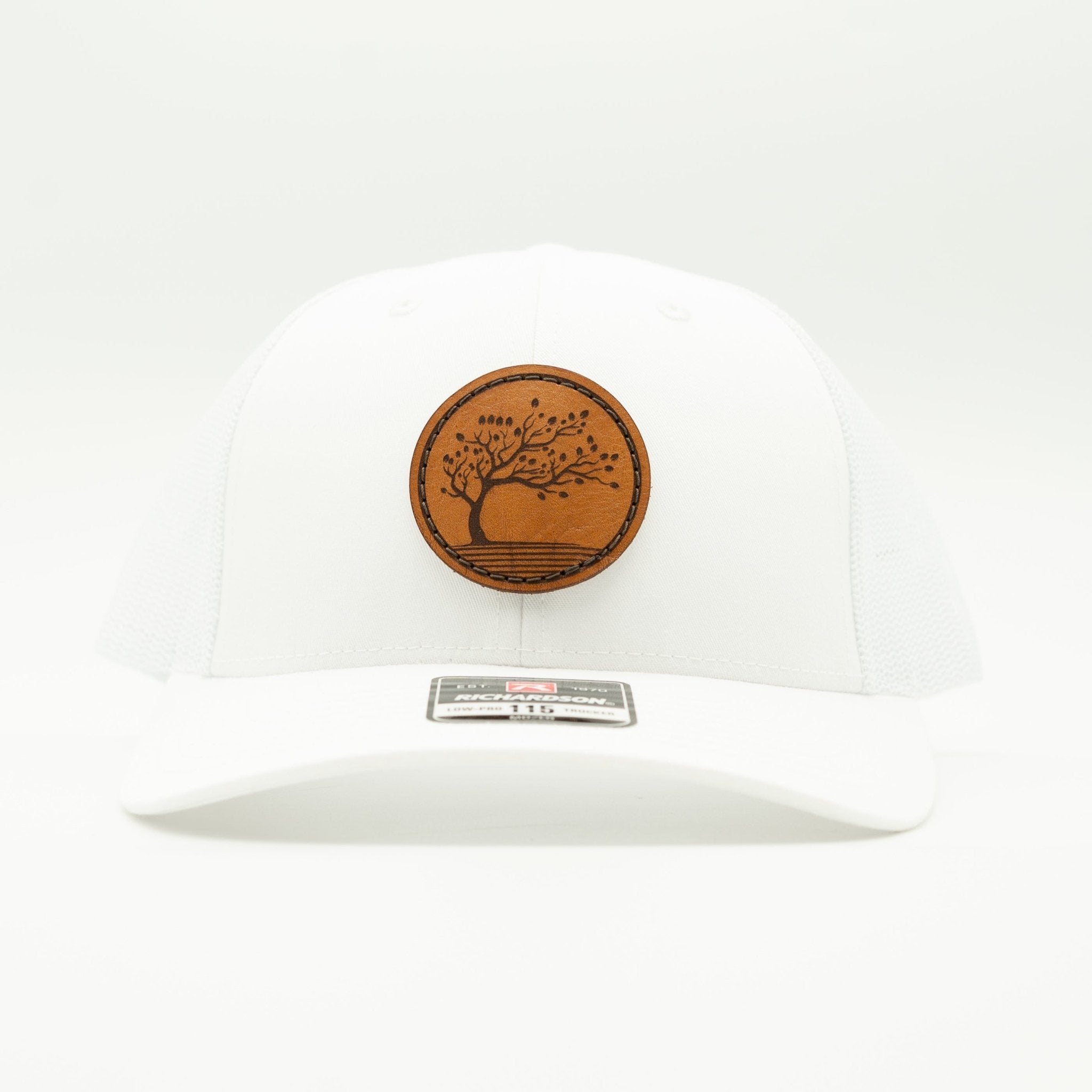 A white structured baseball cap with a curved brim, featuring a circular brown wooden patch with a tree design on the front and a silver metal size tag on the brim.

Color: Solid White