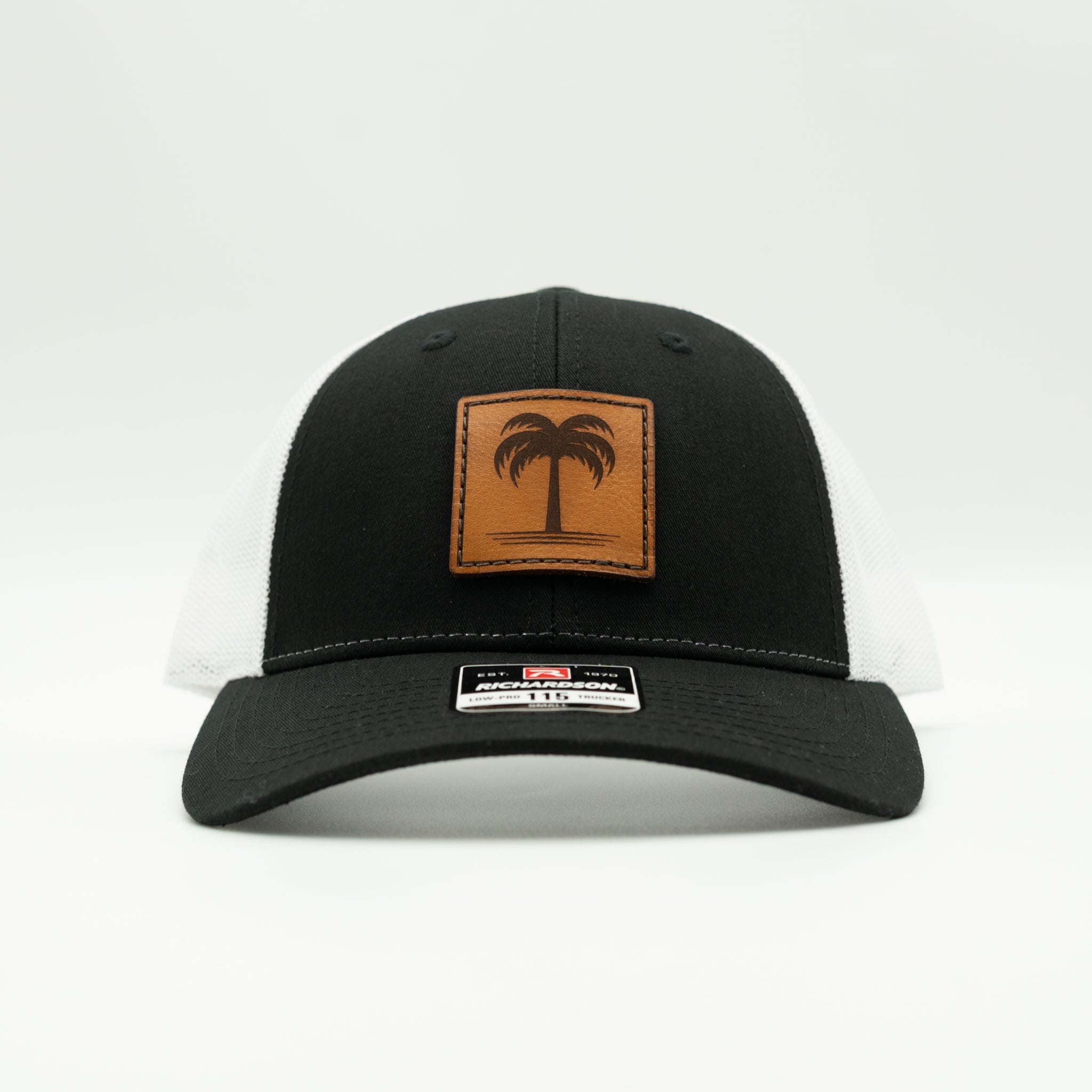 Front view black/white Solo Palm leather patch hat, classic surf-inspired low profile trucker with curved bill and mesh back.
