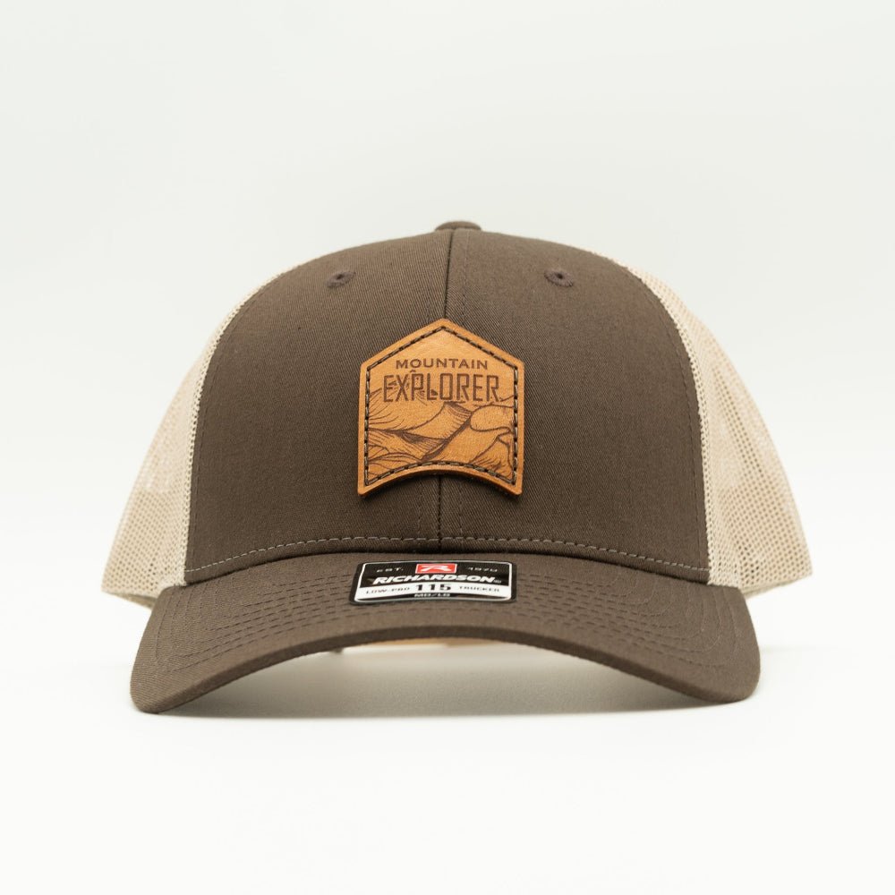 Front view of brown and khaki Mountain Explorer leather patch hat, low profile Richardson 115 trucker with sewn real leather mountain design for classic outdoors style.