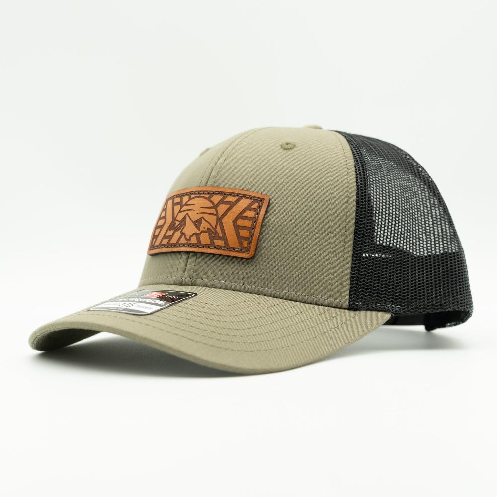A trucker-style baseball cap in khaki green with black mesh back panels and a brown leather patch on the front featuring a stylized logo.

Color: Loden/Black