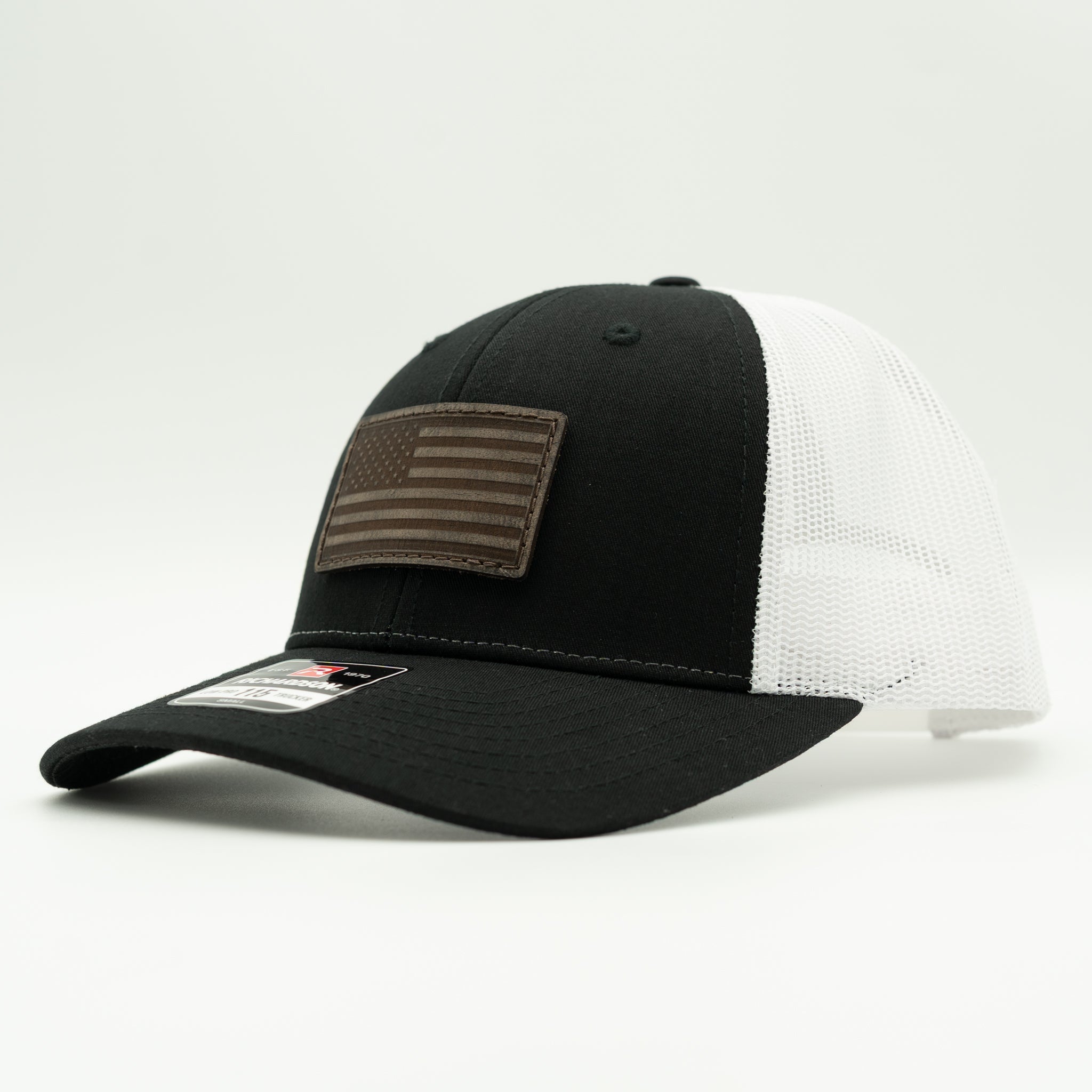 A black and white trucker cap with a brown American flag patch on the front, photographed on a clean white background.

Color: Black/White