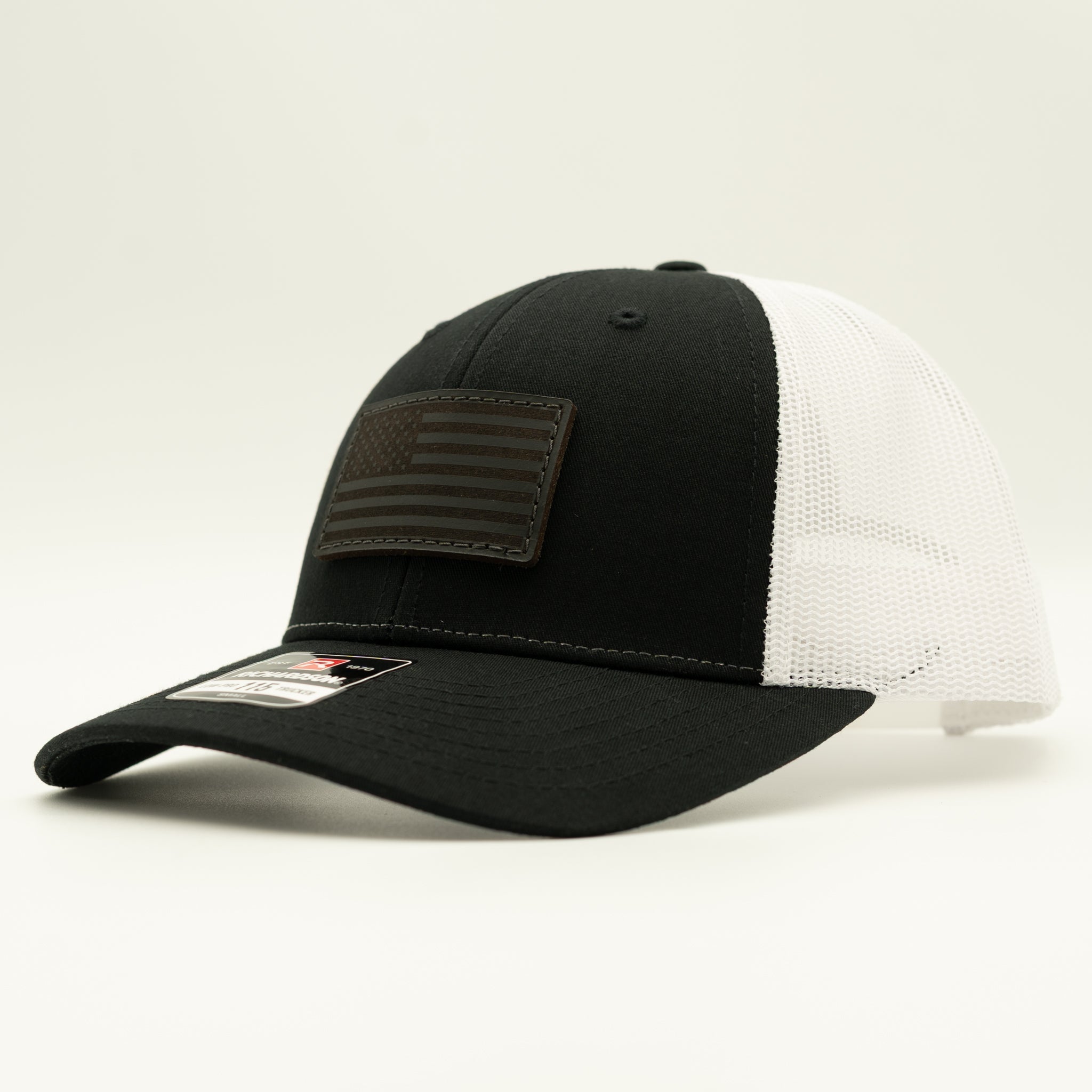 A black and white trucker cap with a black front panel, white mesh back, and a dark brown American flag patch on the front.

Color: Black/White