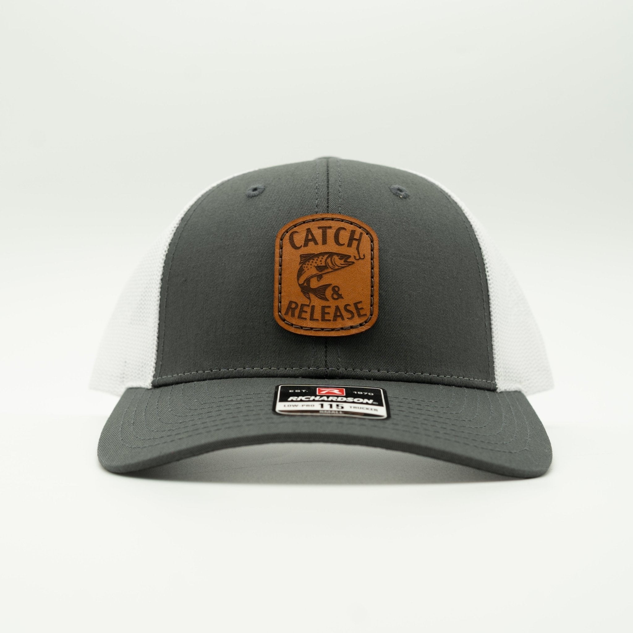 A dark gray and white mesh trucker hat with a brown leather patch on the front that reads 'CATCH RELEASE' with a fish graphic. 

Color: Charcoal/White