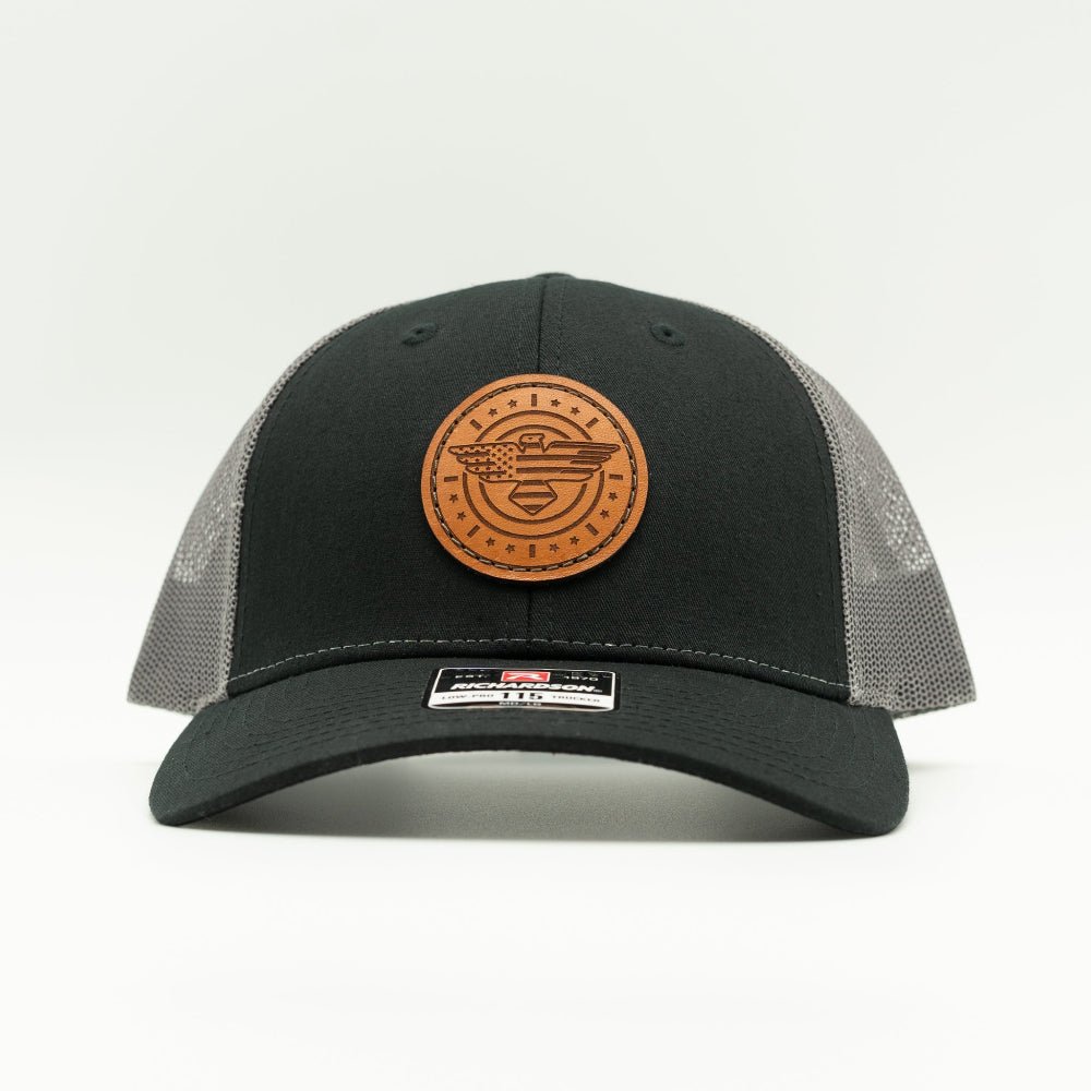 Front view of black and charcoal Richardson 115 low profile trucker hat with round American Eagle and flag leather patch, curved visor, and charcoal mesh back.

Color: Black/Charcoal