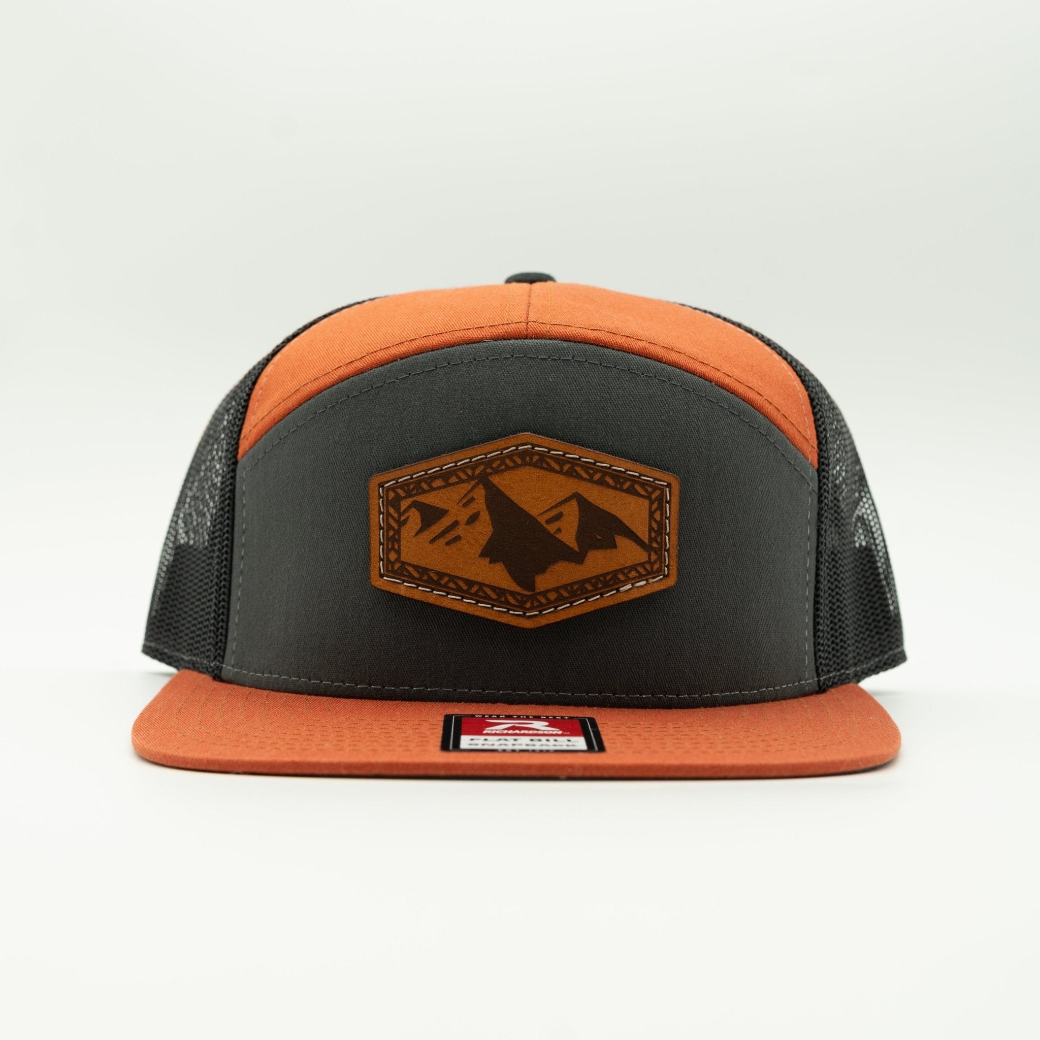 A snapback trucker hat with a dark gray front panel and brim, orange mesh back, and an orange top panel. A brown leather patch with a mountain design is centered on the front.

Color: Charc/Orange/Black 168 (OSFM)