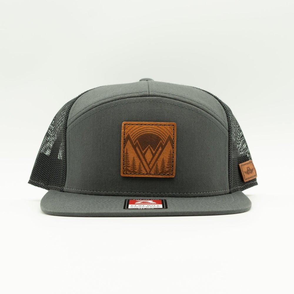 Mountain East leather patch hat on a charcoal and black Richardson 168 seven panel trucker, front view showing flat bill, high crown, mesh back, and stitched leather mountain patch.