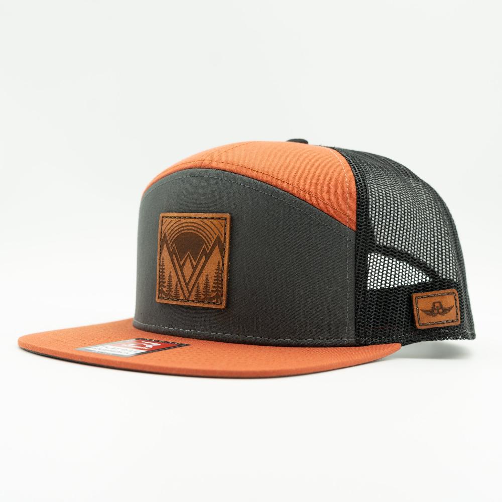 Side view of Mountain East leather patch hat on charcoal, orange, and black Richardson 168 flat bill trucker, showing sewn leather mountain patch, orange bill, and mesh back.