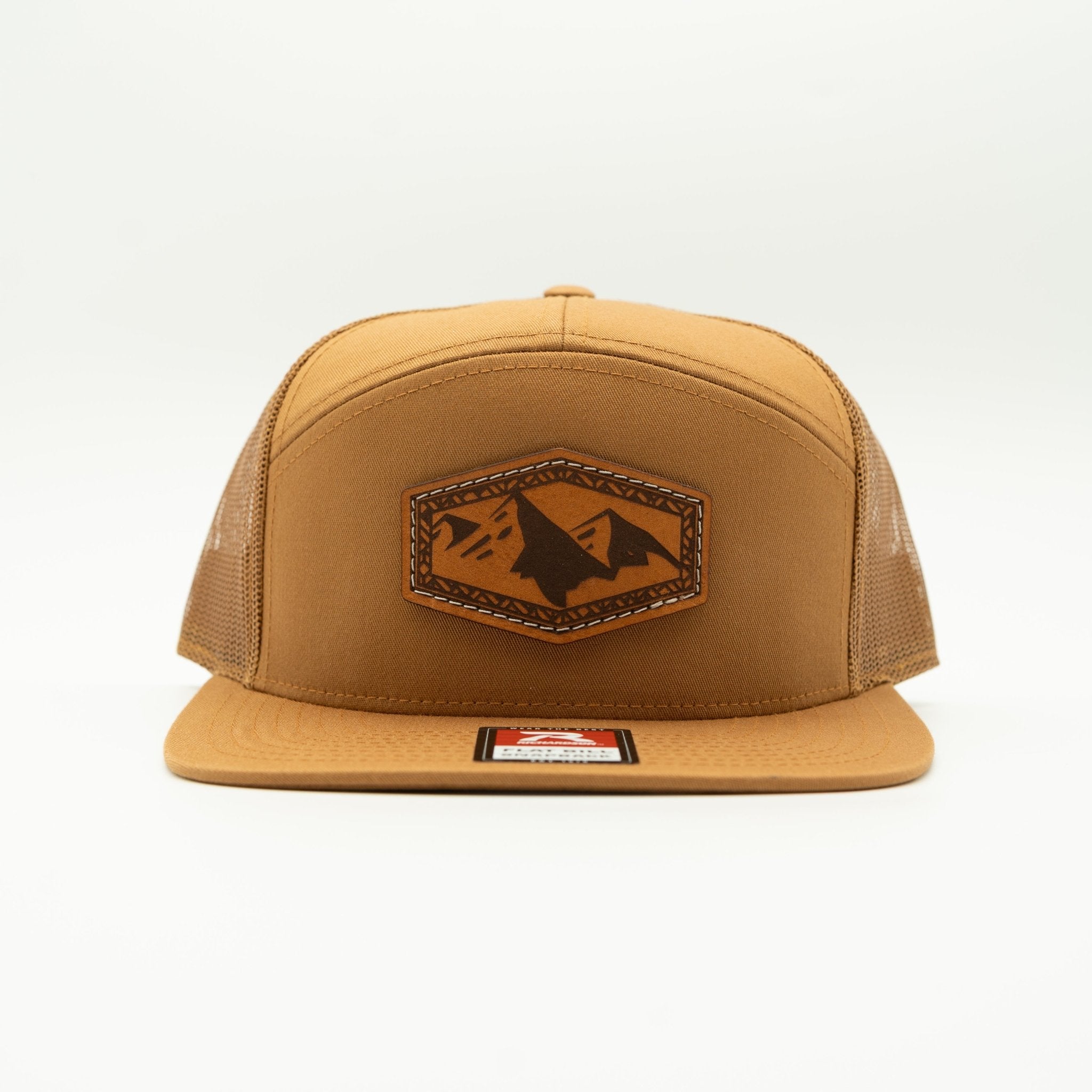 A tan trucker hat with a brown leather patch on the front featuring a mountain and wolf design, set against a plain white background.

Color: Caramel 168 (OSFM)