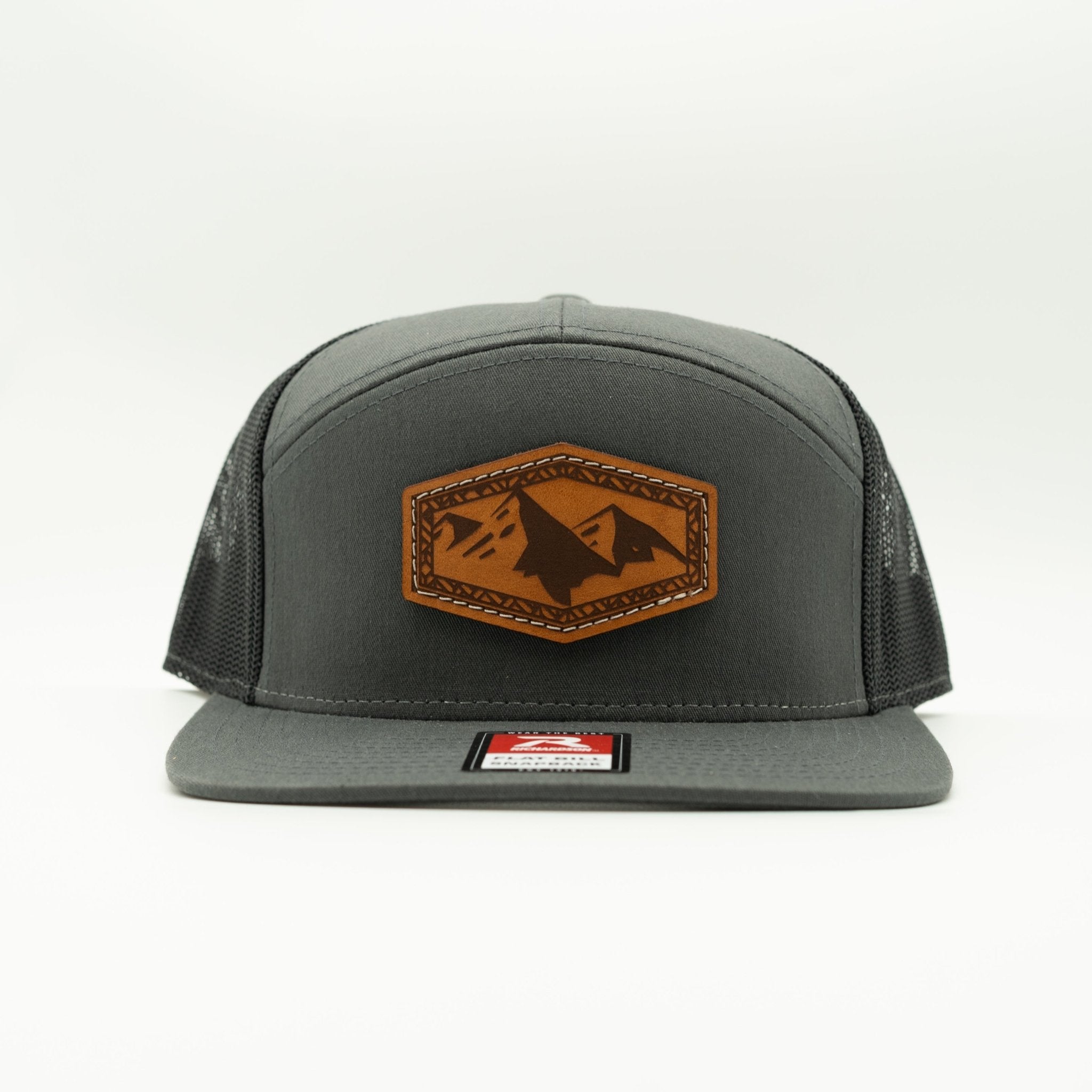 A dark gray trucker hat with a brown leather patch on the front featuring a mountain design, set against a plain white background.

Color: Charcoal/Black 168 (OSFM)