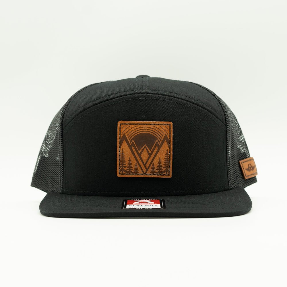 Mountain East leather patch hat on a solid black Richardson 168 seven panel trucker, front view showing flat bill, high crown, mesh back, and stitched veg tanned mountain patch.