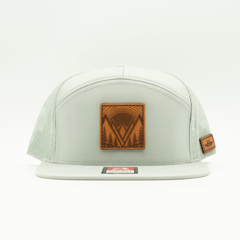 Mountain East leather patch hat on a quarry gray Richardson 168 seven panel trucker, front view showing flat bill, high crown, mesh back, and stitched veg tanned mountain patch.
