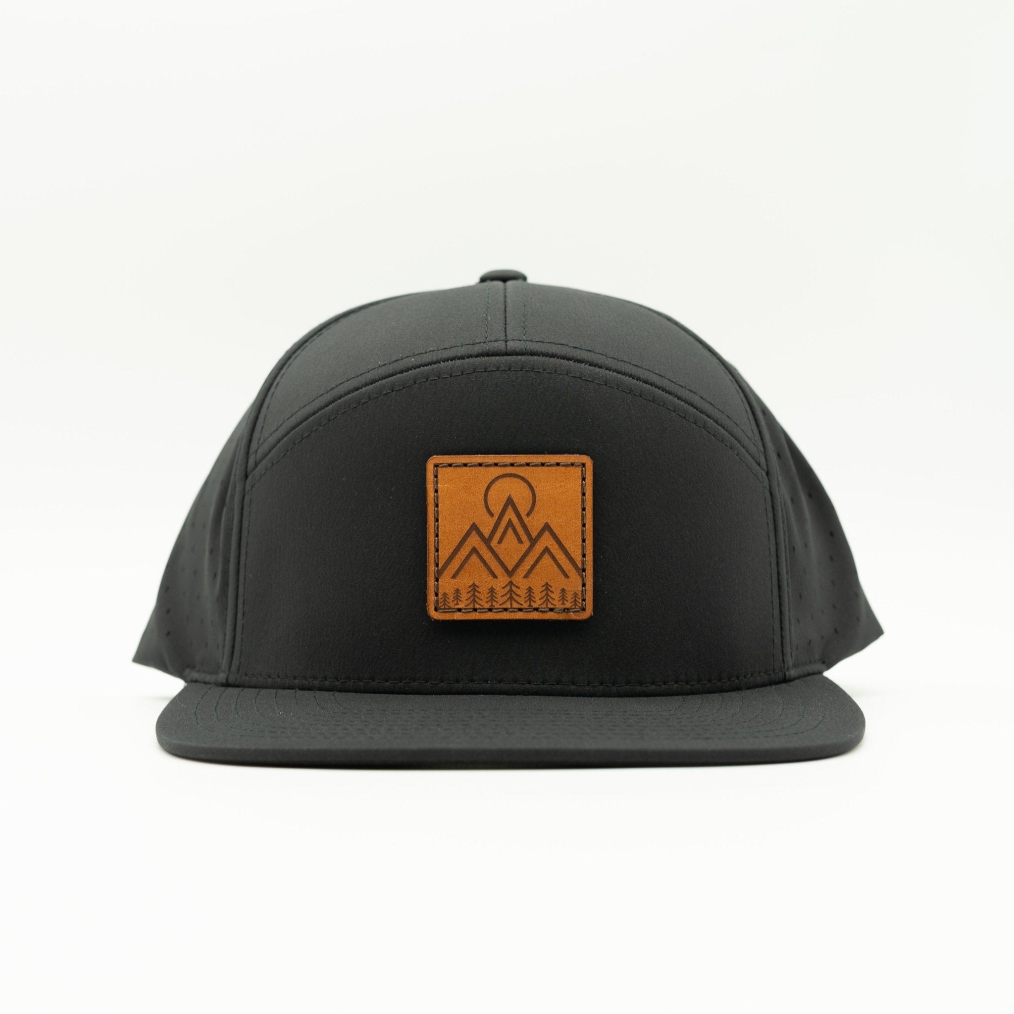 A black flat-brim cap featuring a square brown leather patch on the front with a mountain and tree logo, set against a plain white background.

Color: Black