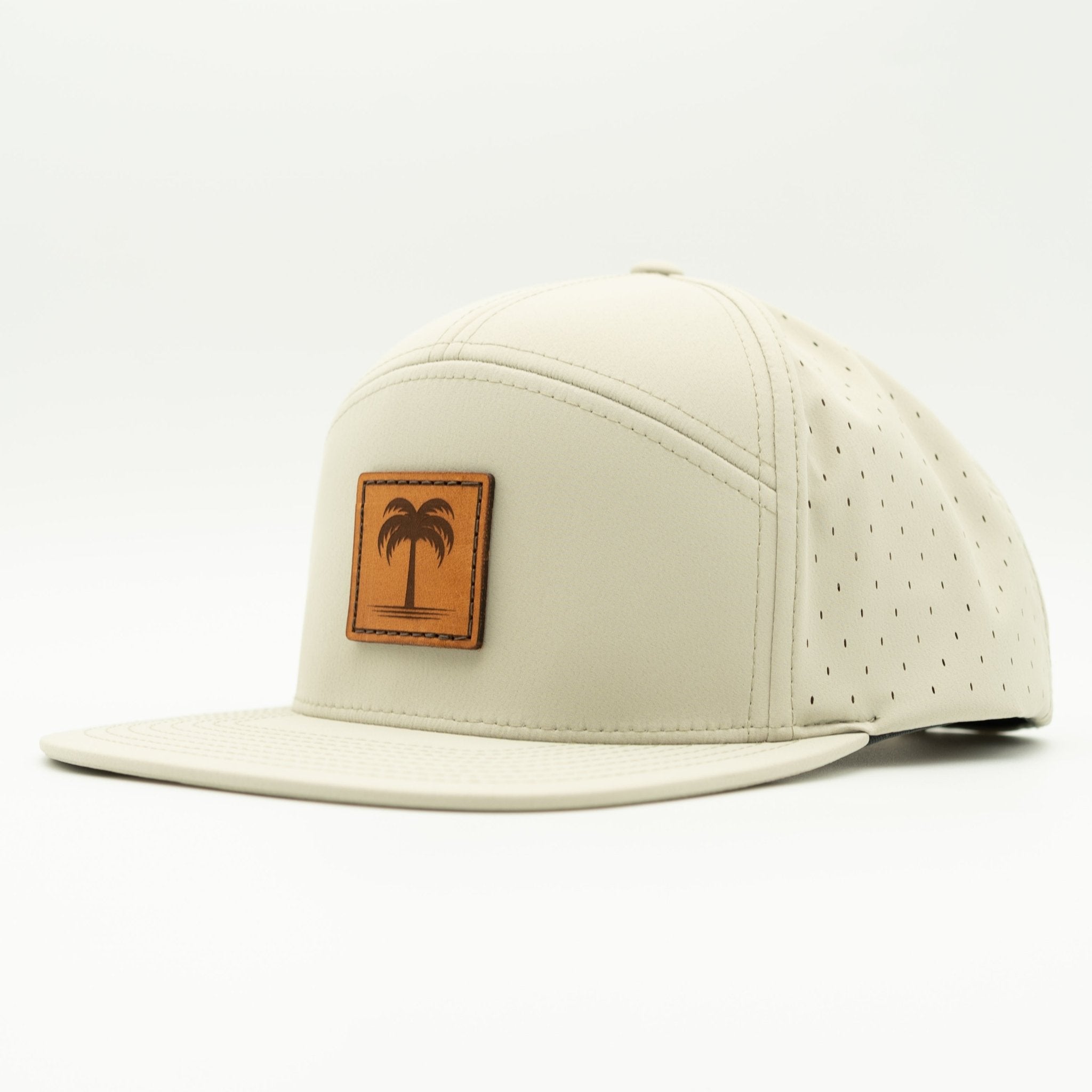 A light beige 5-panel cap with a flat brim, featuring a brown leather patch on the front with a palm tree logo, set against a plain white background.

Color: Ivory